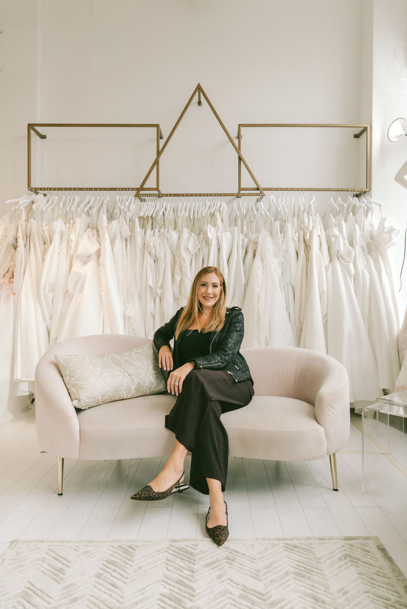 Elegant bridal boutique interior with white dresses displayed on racks and a modern cream-colored couch.