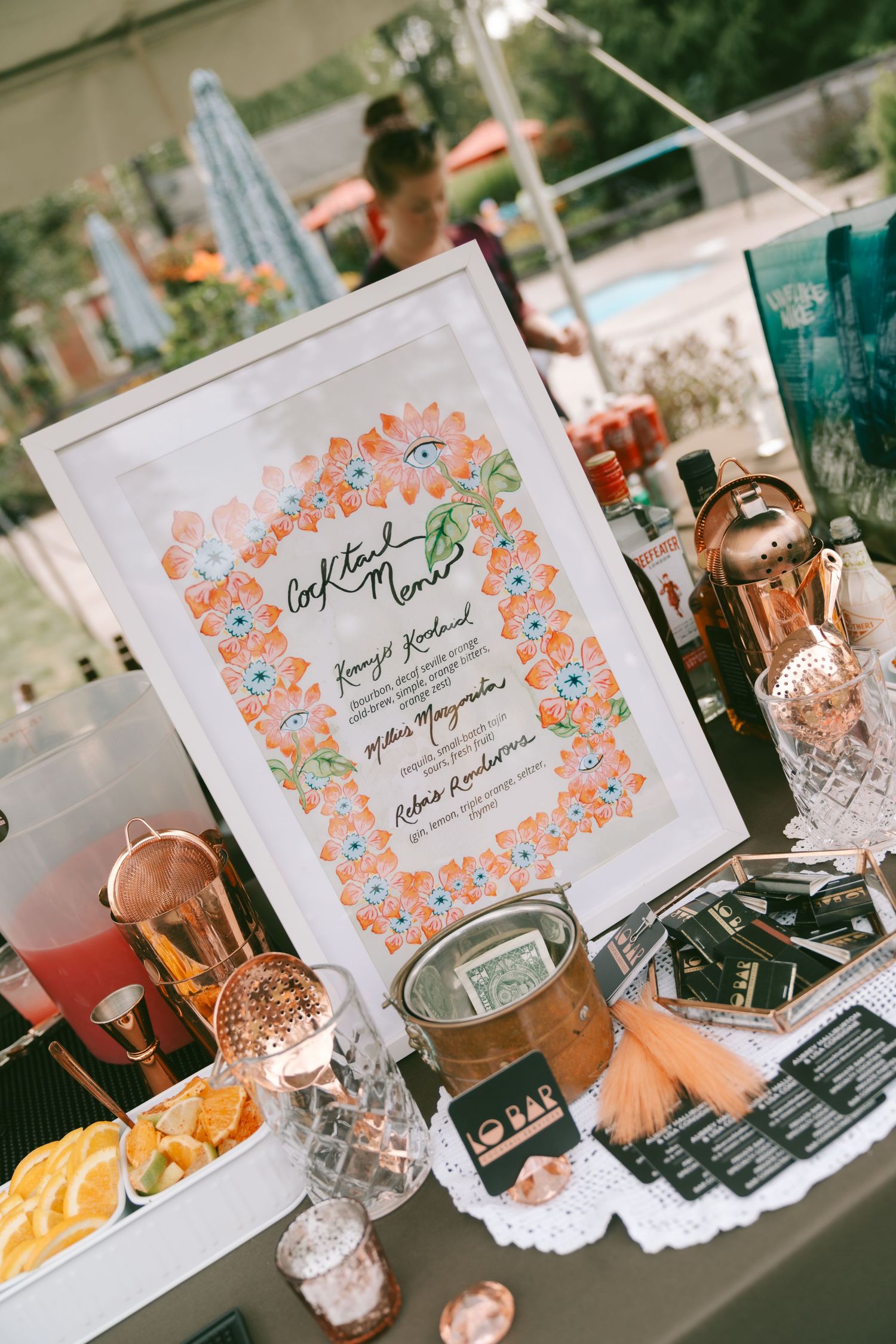 Wedding reception table displays feature floral-framed signs and decorative elements in coral and white color scheme.
