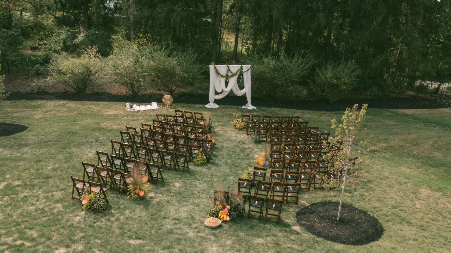 Wide shot of wooden chairs set up for an outdoor wedding ceremony with fall decorations.