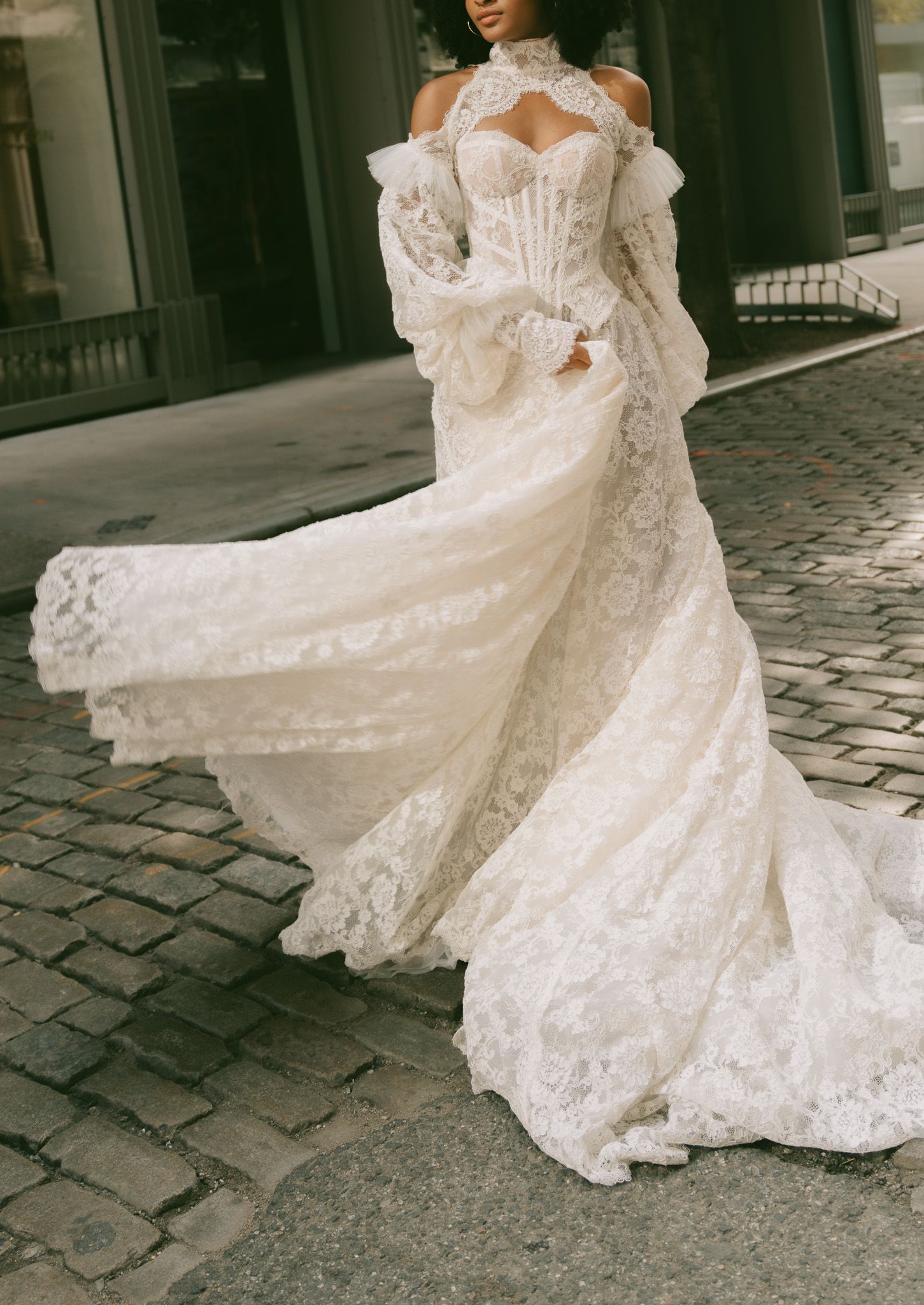 Ornate off-shoulder Galia Lahav lace wedding gown with flowing lace train on cobblestone street in NYC.