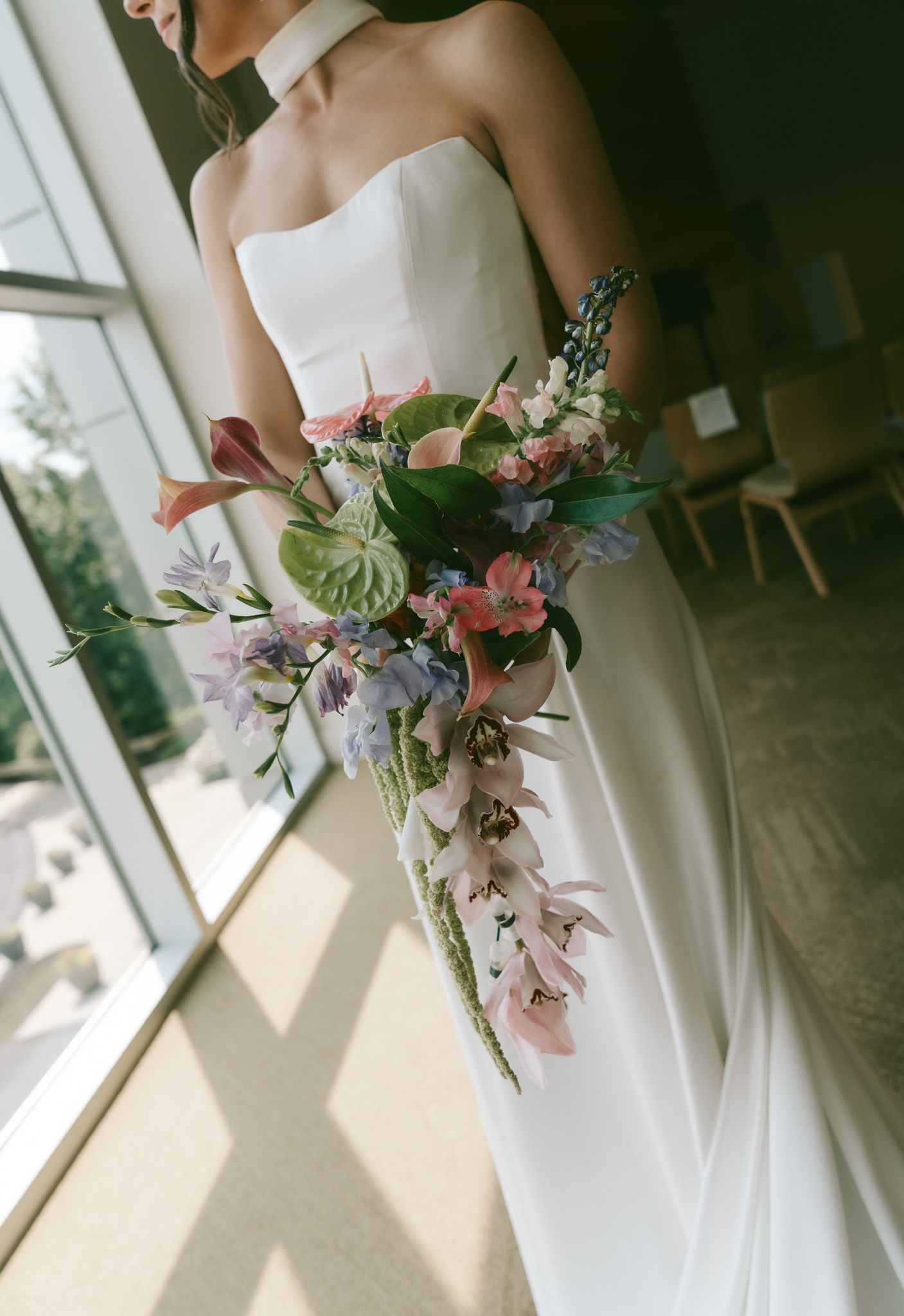 Elegant white wedding dress detail with delicate floral bouquet near sunlit window.