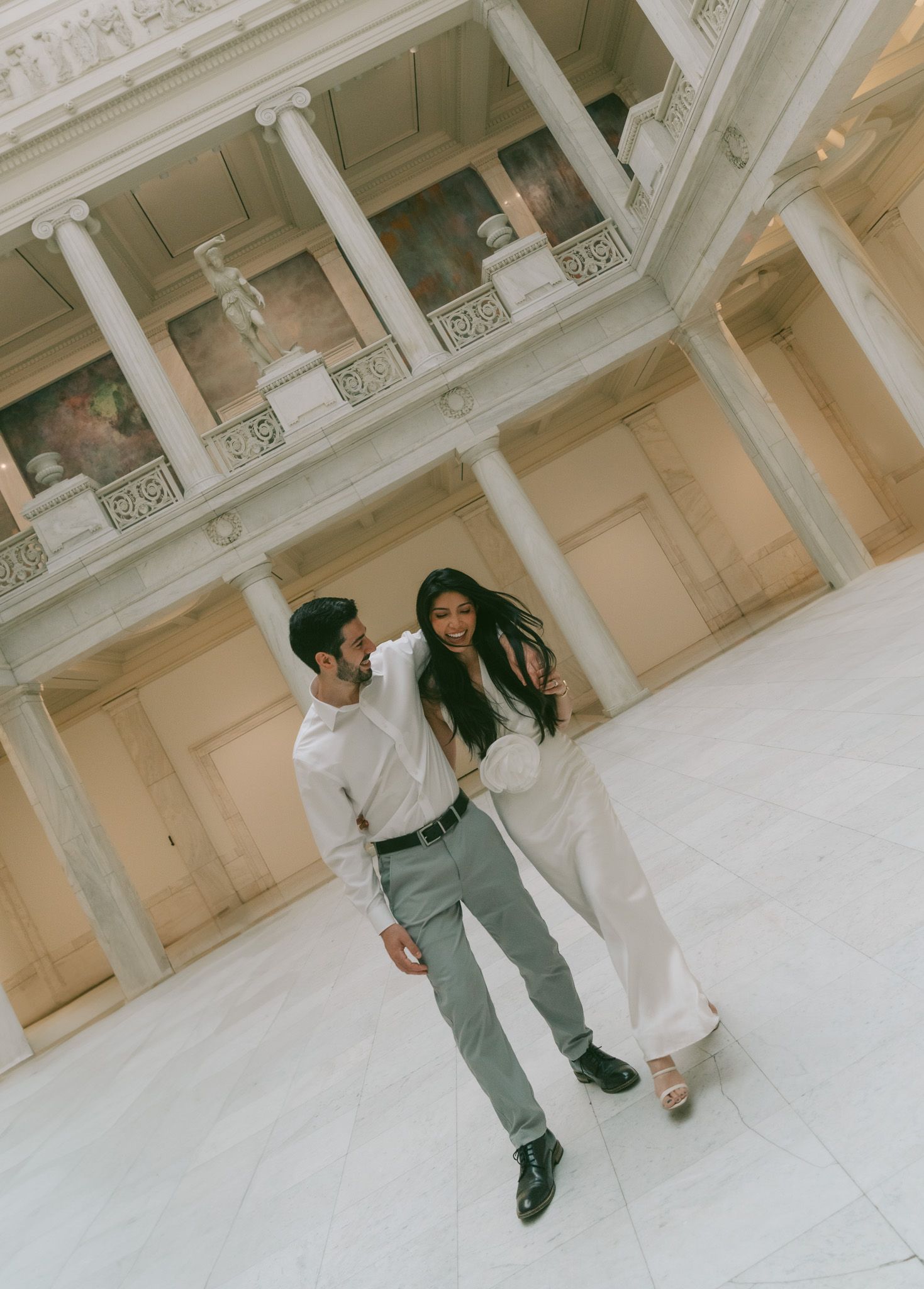 A couple shares a tender moment in an ornate architectural setting with white columns.