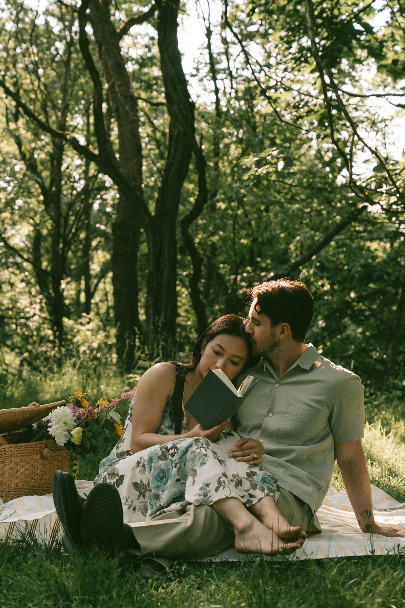 Couple enjoying a romantic picnic date laying on a blanket in a sunlit forest setting with flowers and a basket at shenley park, pittsburgh.