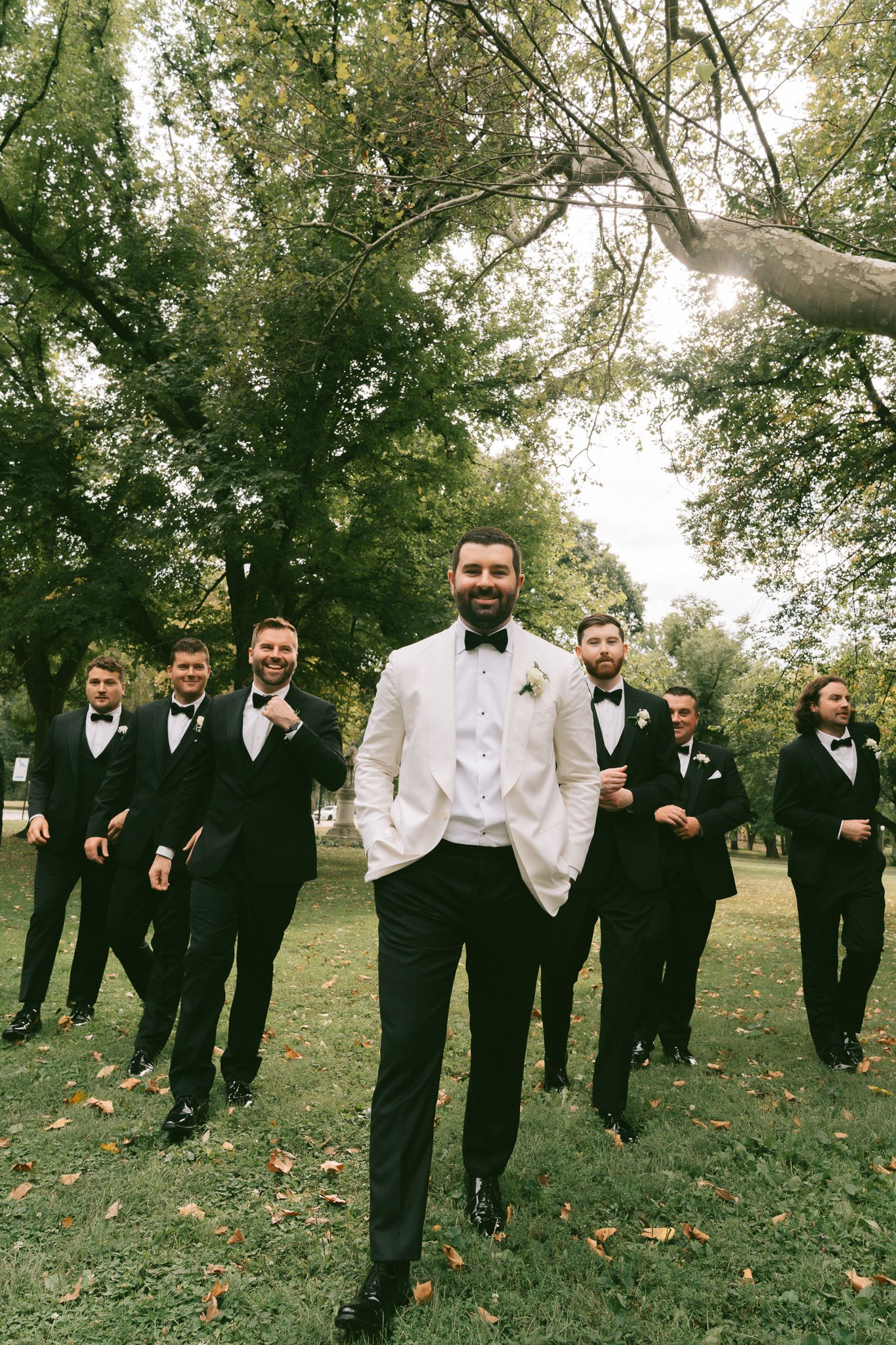 Wedding party poses outdoors with groomsmen in black suits behind groom in white jacket on autumn day in downtown pittsburgh, pa.