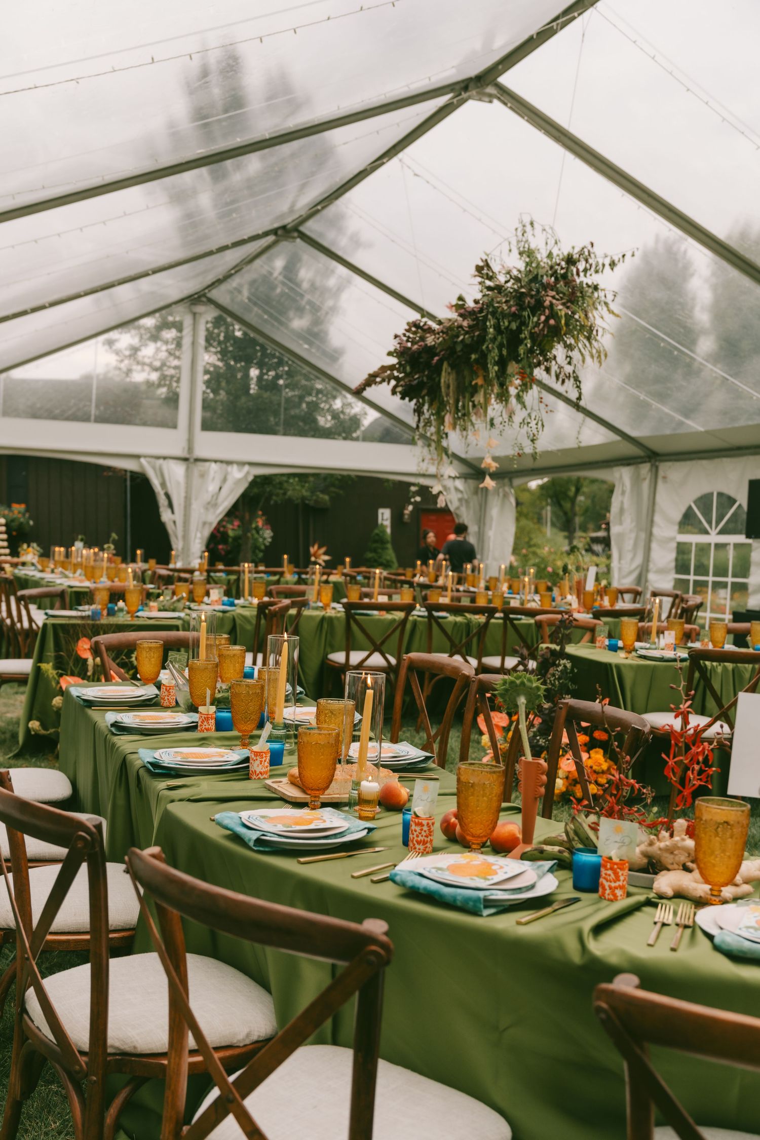 Elegant wedding reception tent with long tables decorated in green linens and orange floral centerpieces.