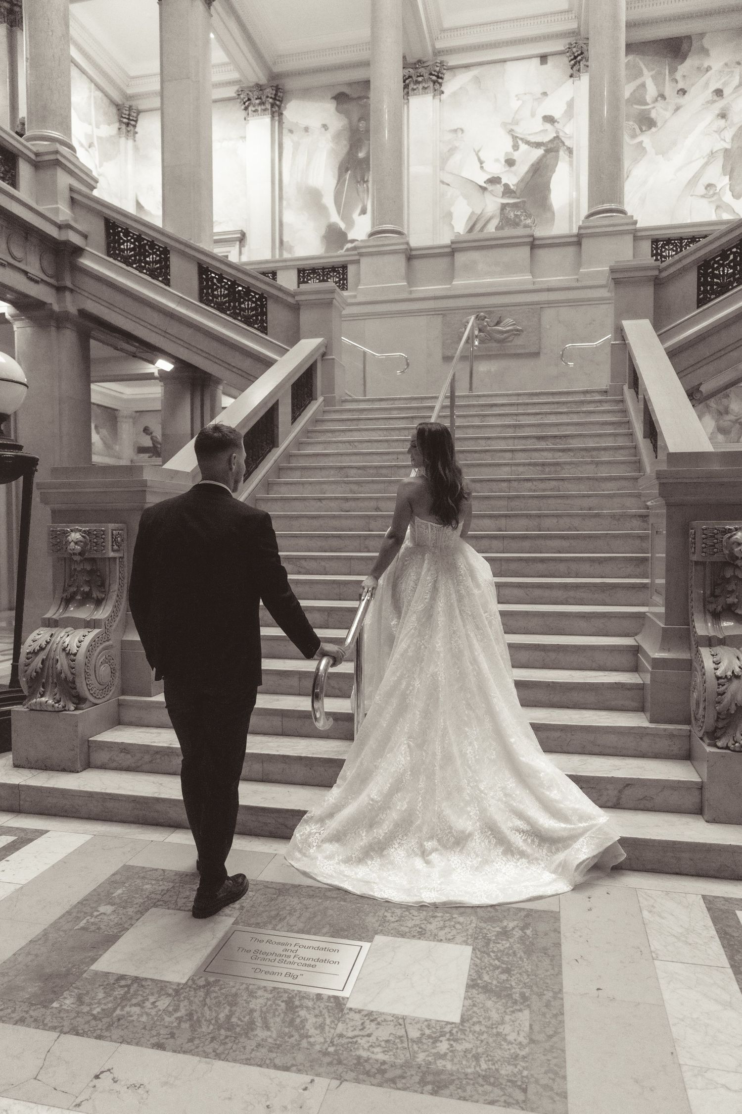 A couple in wedding attire ascends an elegant marble staircase in a series of black and white photographs.
