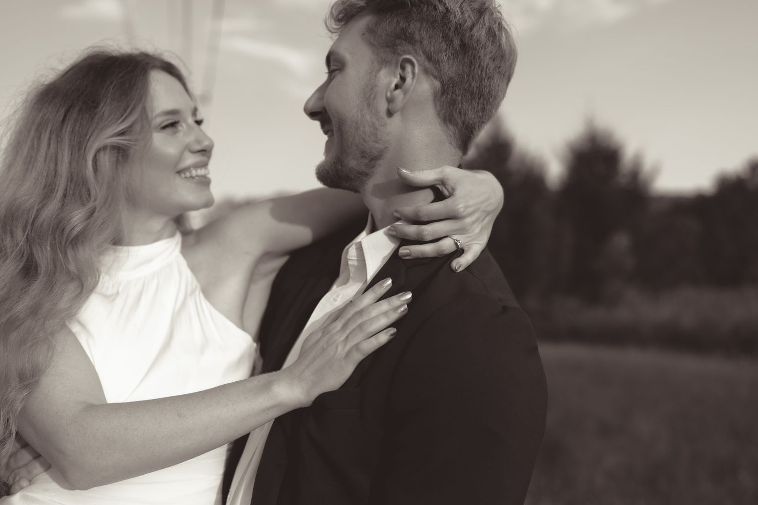Candid moment of a couple laughing and embracing outdoors in black and white.