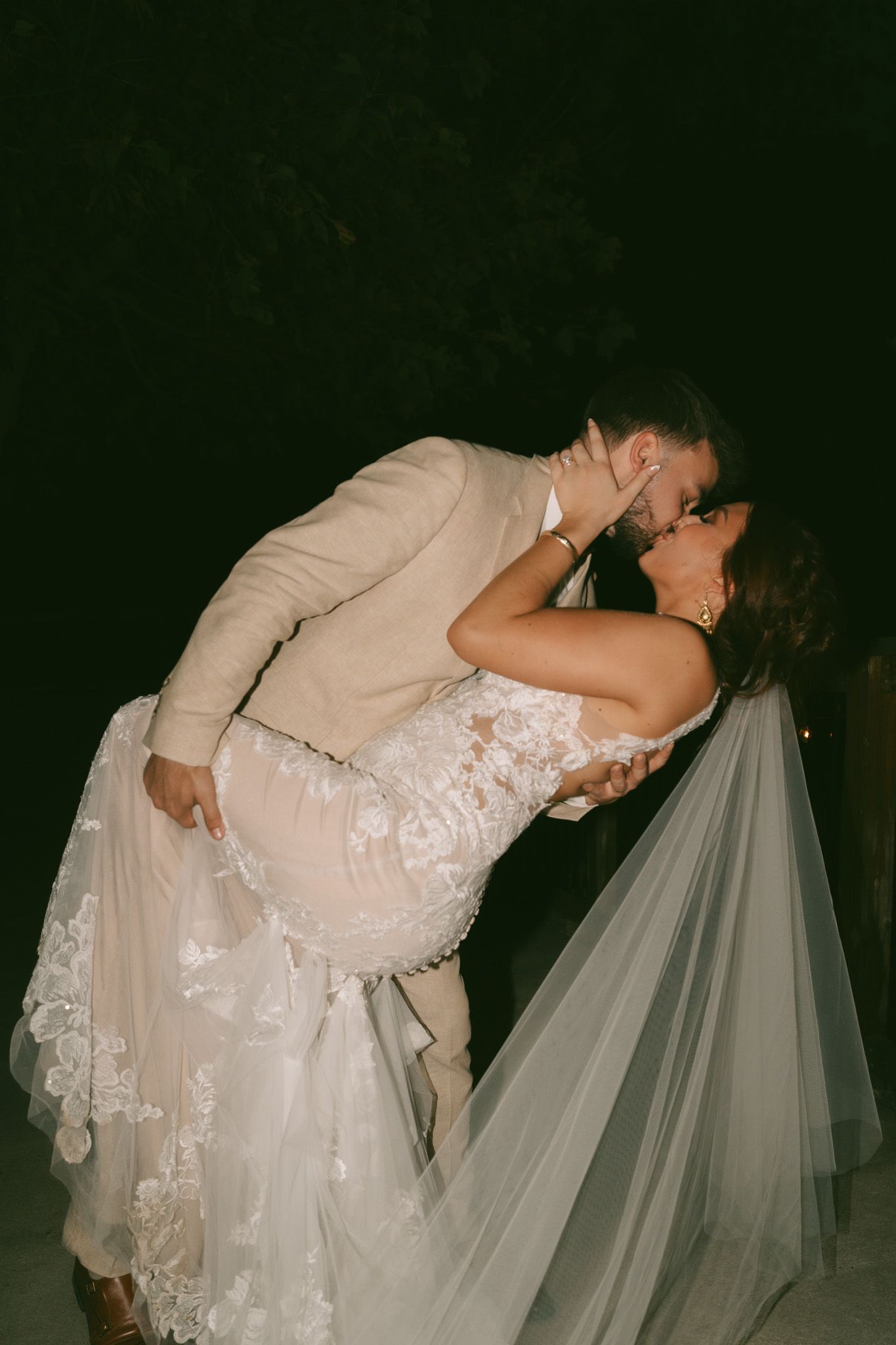 Couple in wedding attire sharing romantic dip kiss at night.