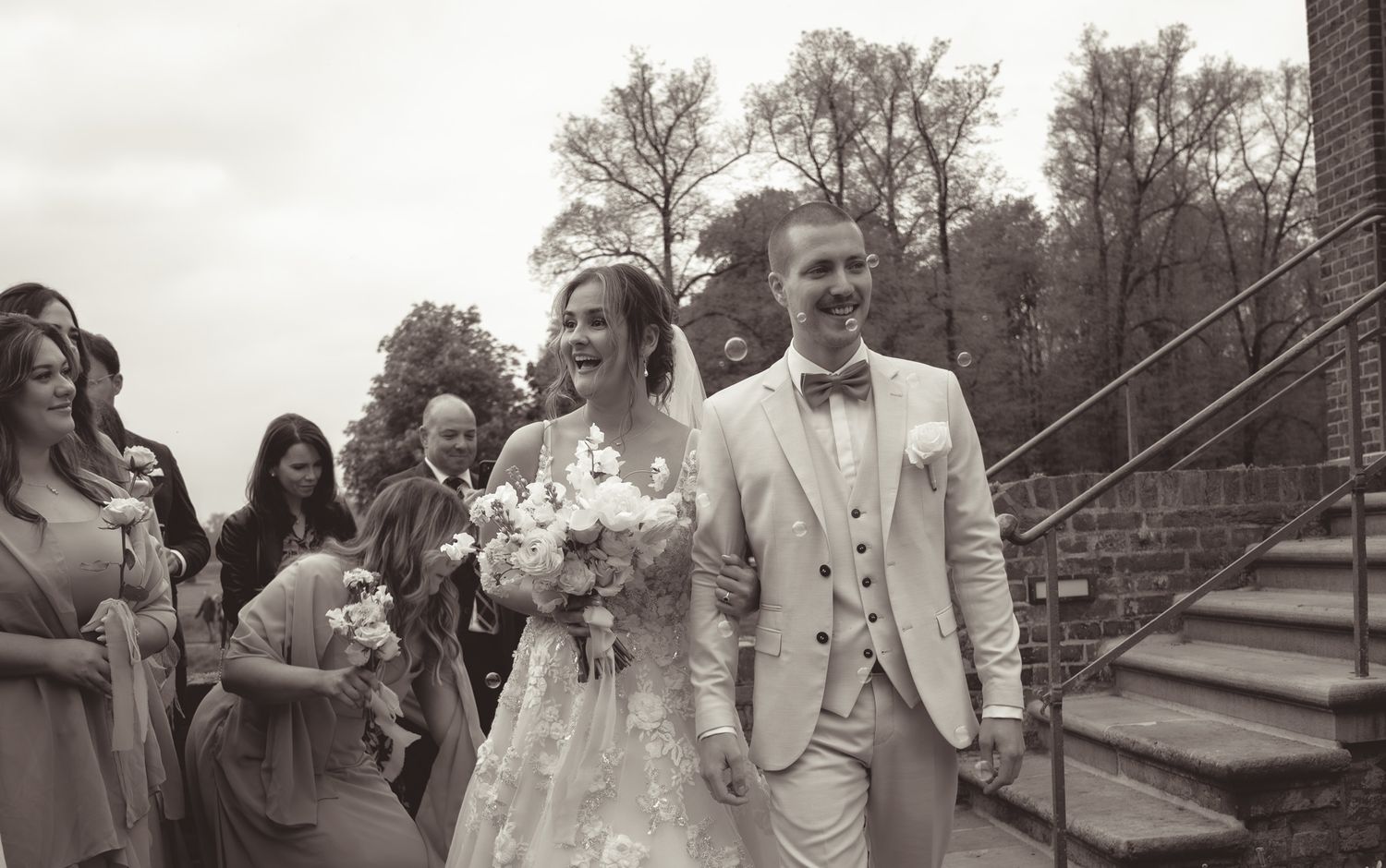 Wedding party exits ceremony venue on brick pathway under cloudy skies in Germany.
