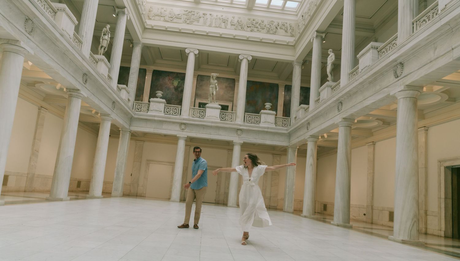 Grand interior hall of a historic building with ornate white columns and a glass ceiling letting in natural light.
