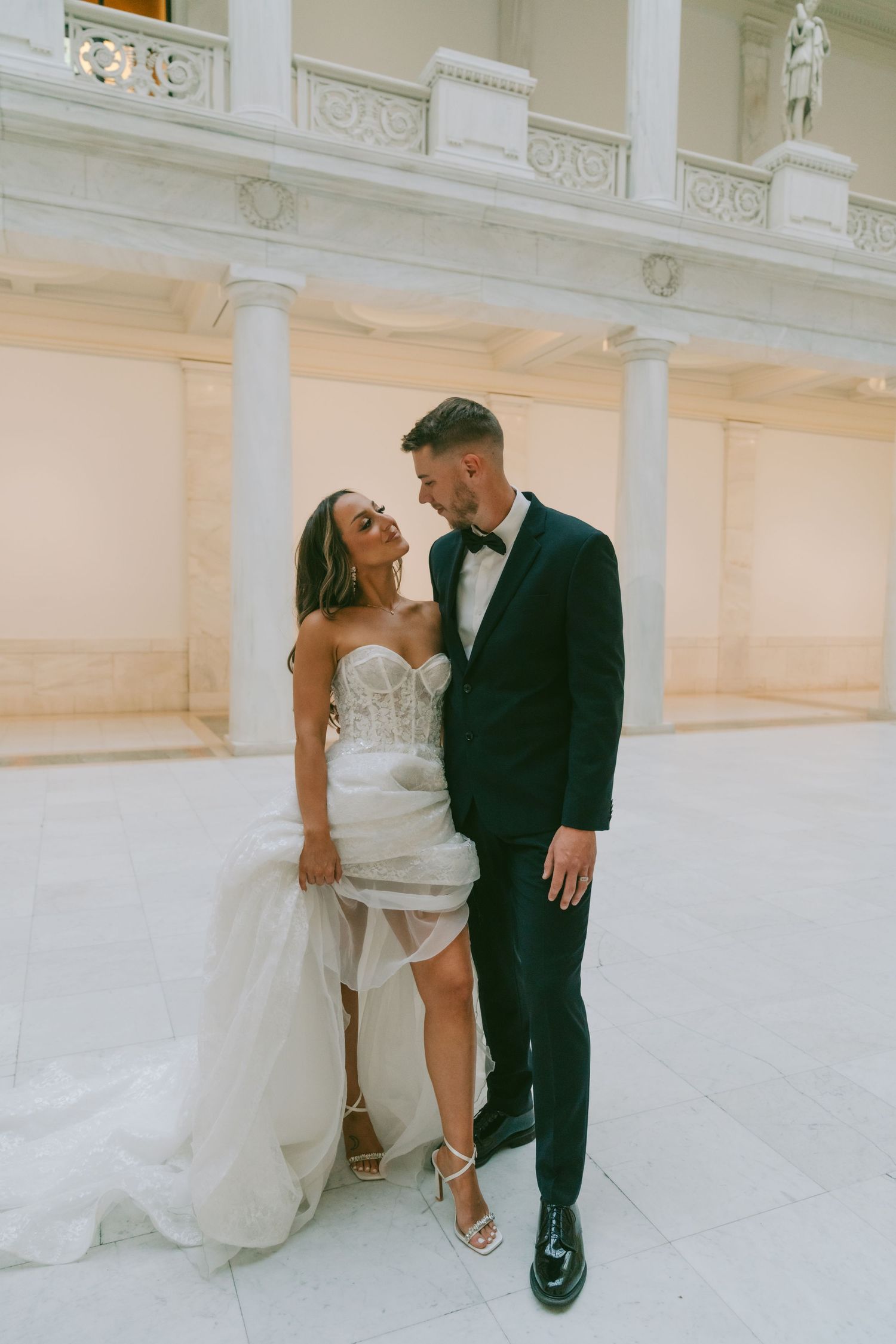 A couple shares an intimate moment against a white columned wall in wedding attire.