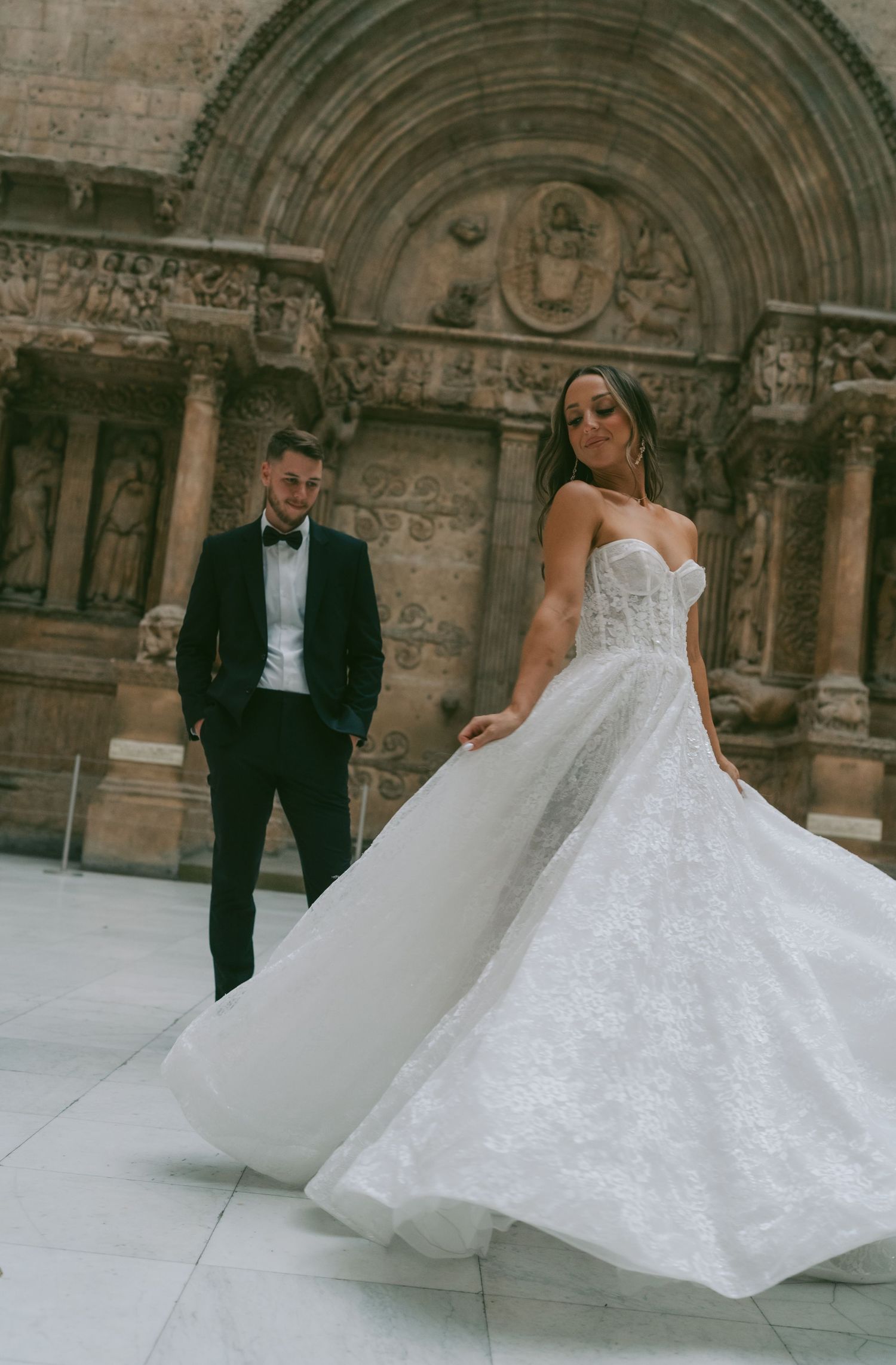 A stunning wedding photo showcasing an elegant white bridal gown and classic tuxedo against ornate cathedral architecture.