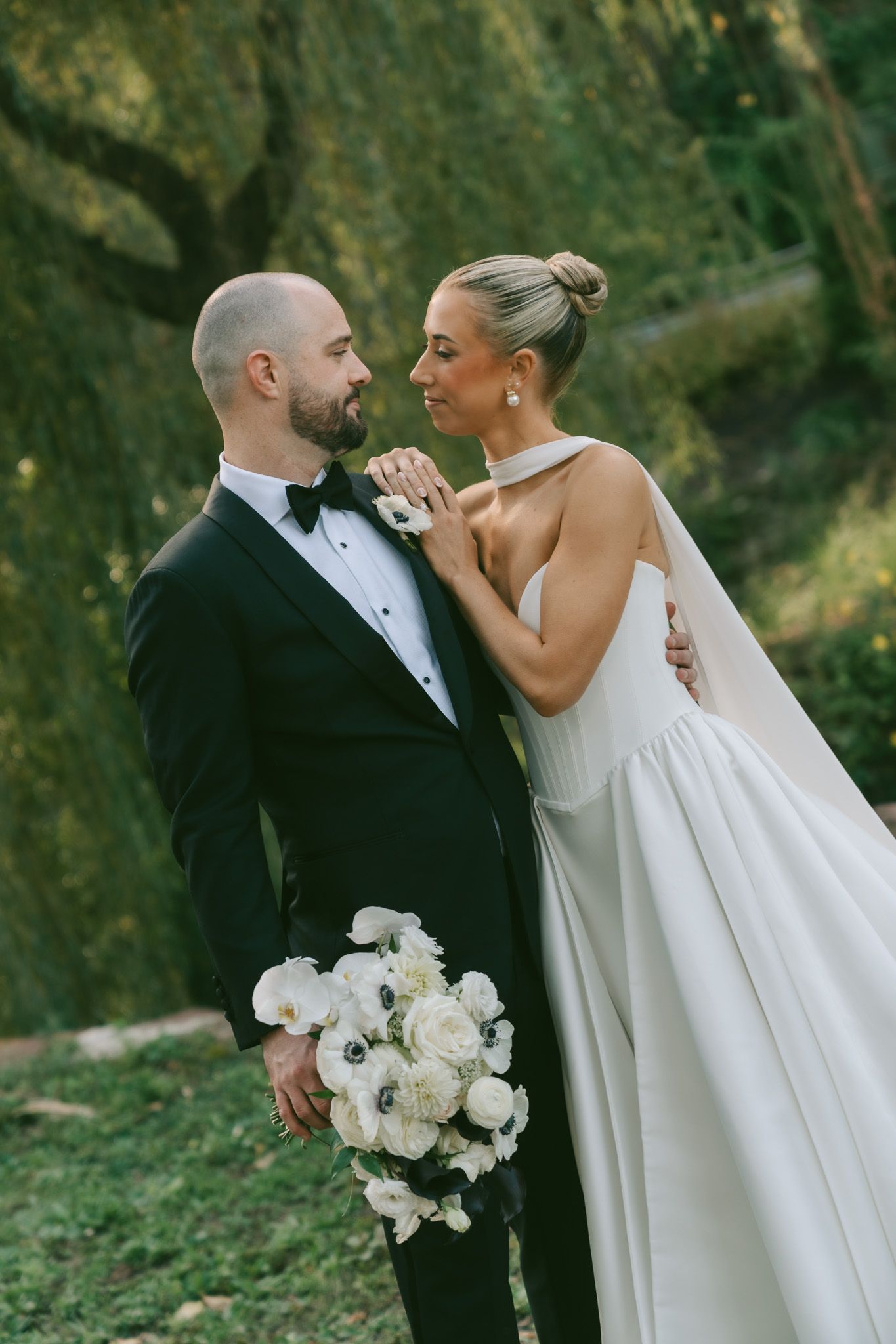 A couple shares an intimate moment during their wedding photoshoot in a lush outdoor garden setting.