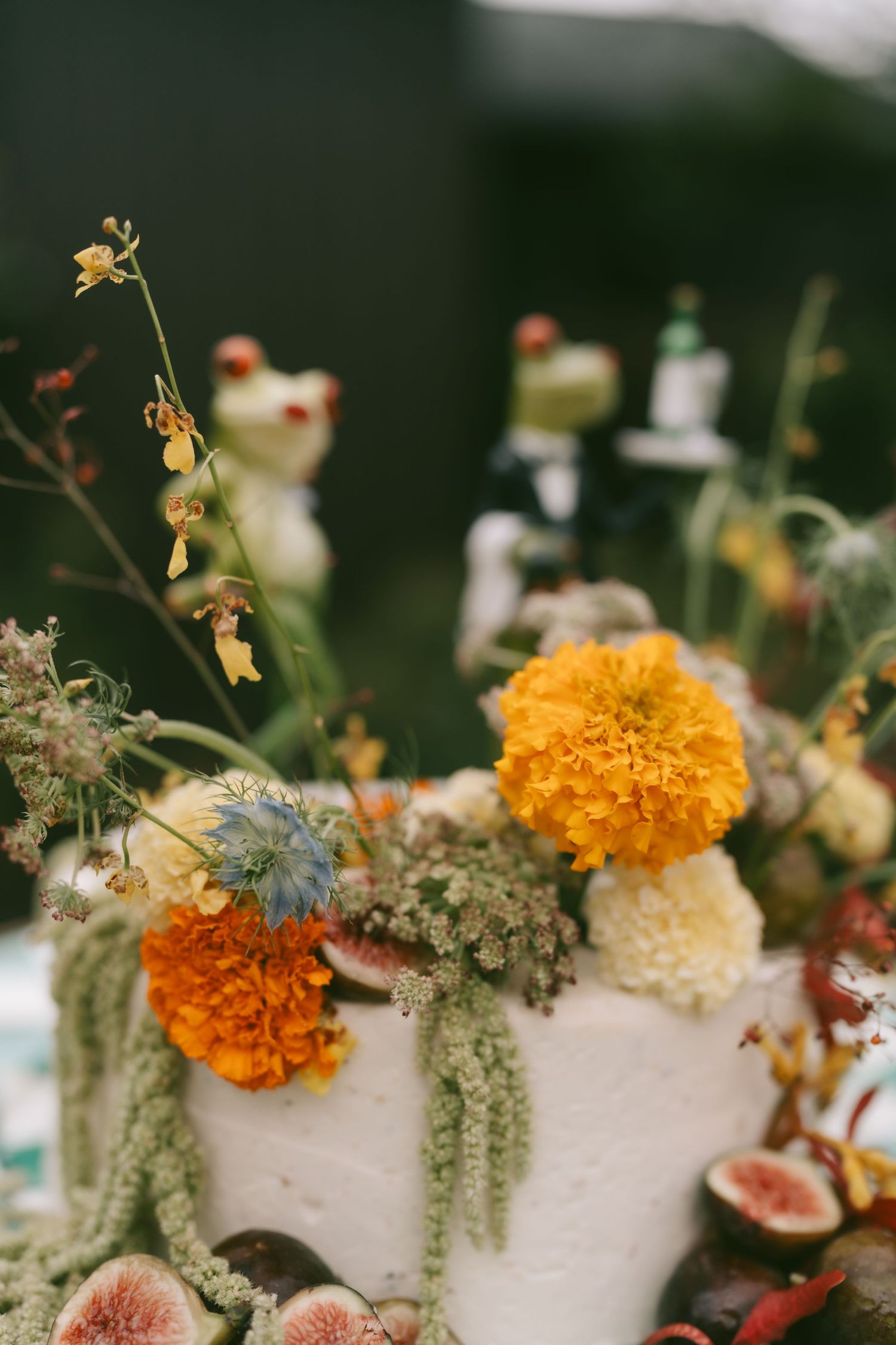 Wedding cake decorated with orange marigolds and greenery against a dark background.