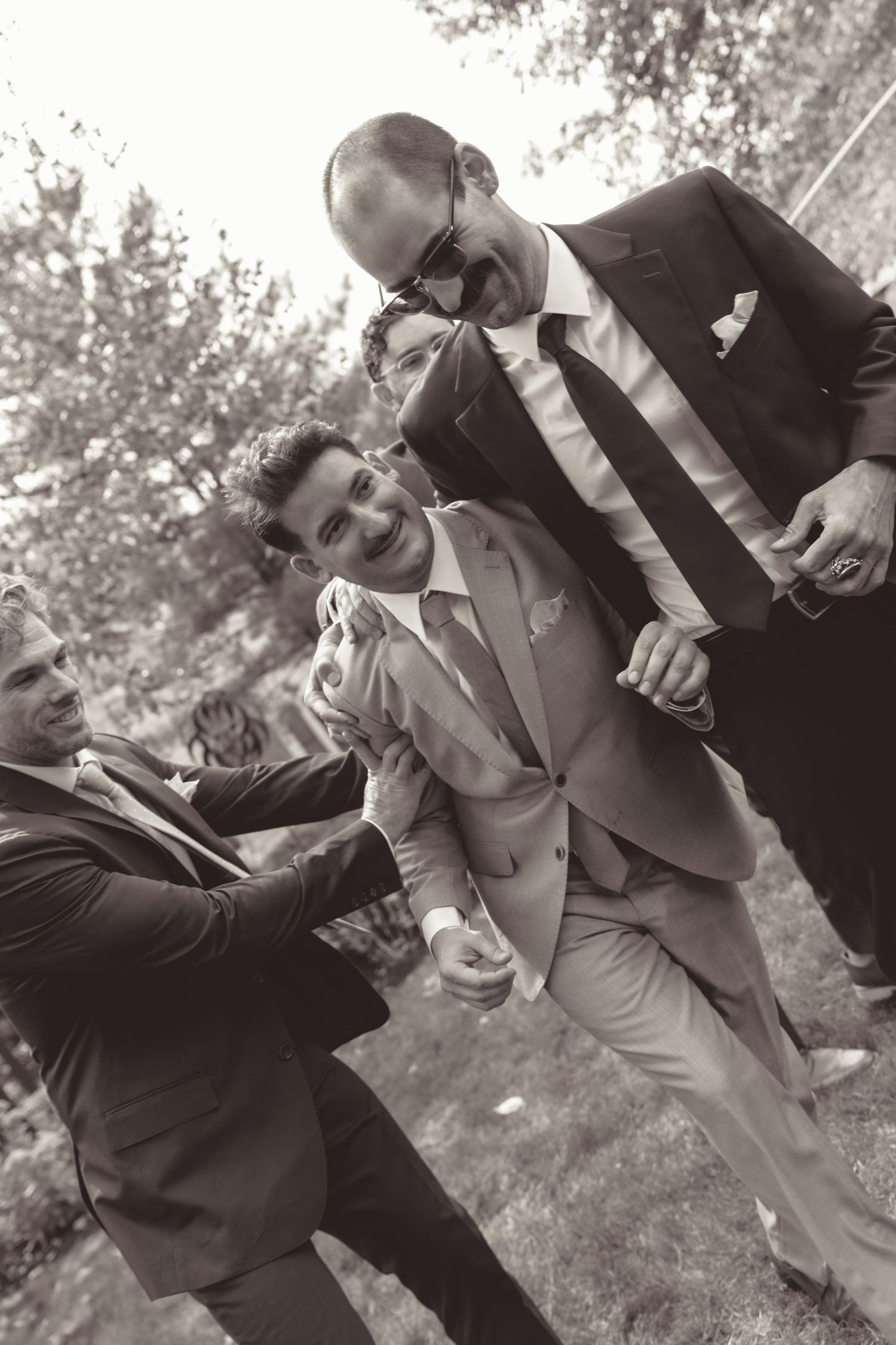 A black and white sequence showing groomsmen in suits playfully posing together outdoors.