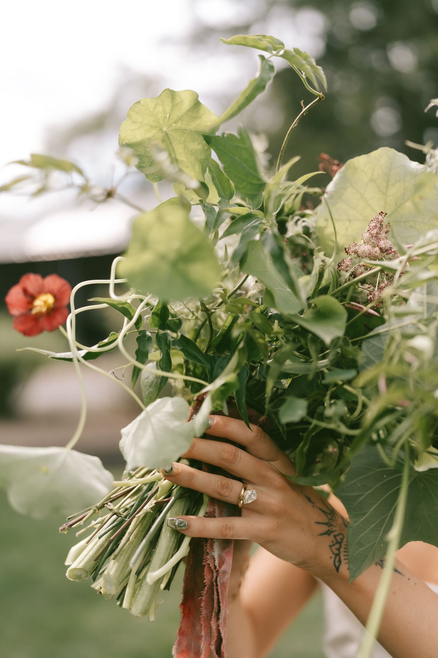 Close-up of hands holding a rustic floral bouquet with green foliage and red flowers.