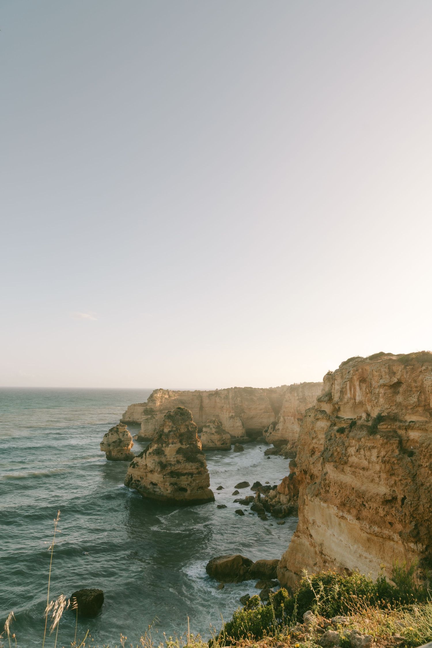 Golden limestone cliffs rise above turquoise Atlantic waters at Ponta da Piedade, Lagos, Algarve, Portugal at sunset.