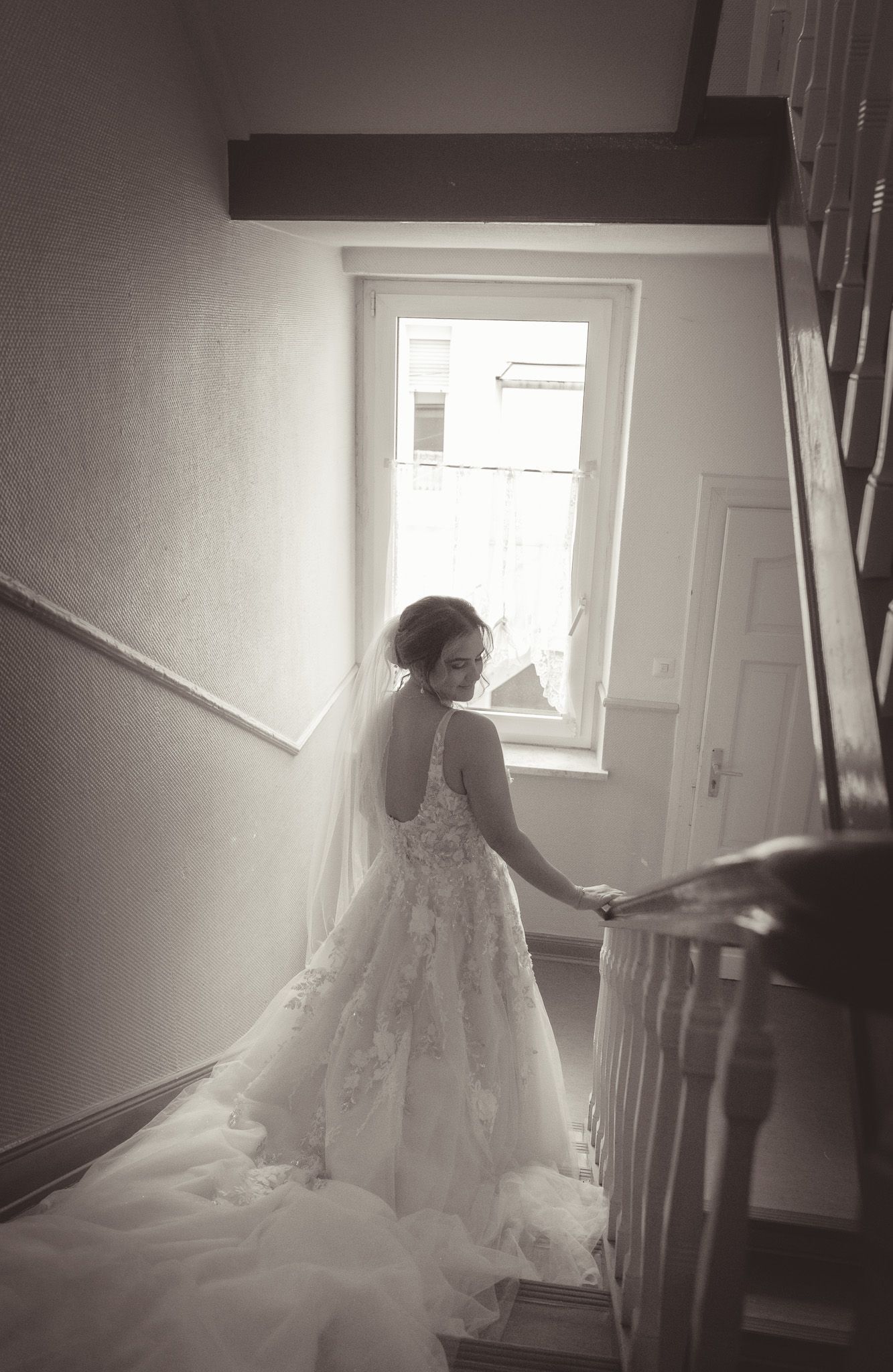 A wedding dress silhouette against a bright window in a stairwell creates a romantic atmosphere in Germany.