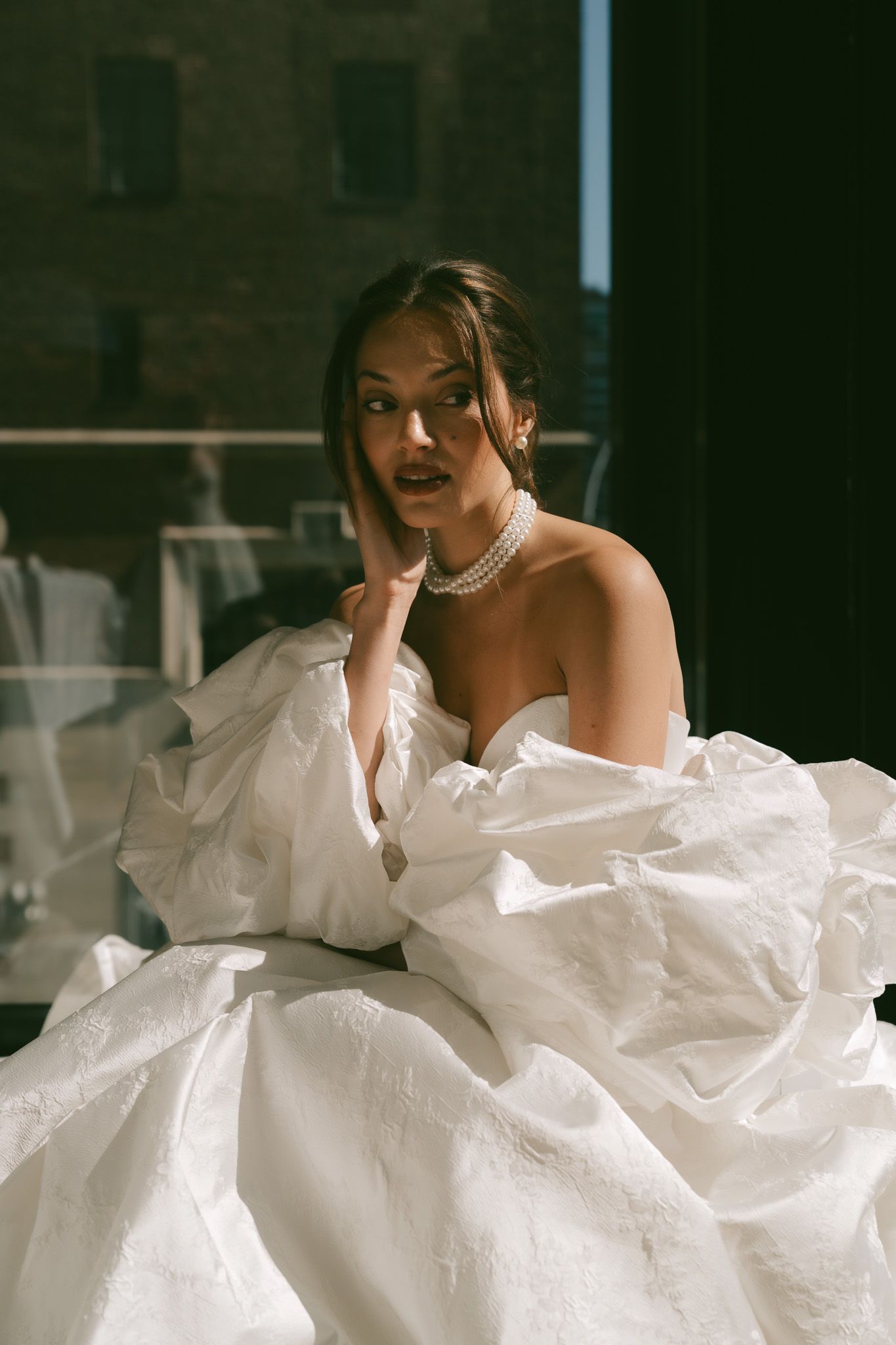 Woman in flowing white dress lounging gracefully against light background in artistic portrait series.