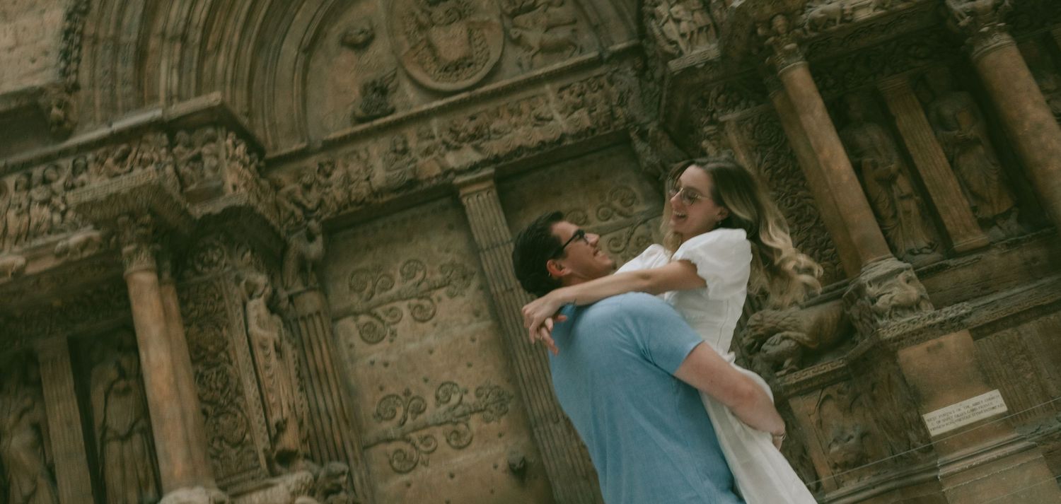 A couple shares a romantic kiss while standing in front of ancient stone ruins and architecture.