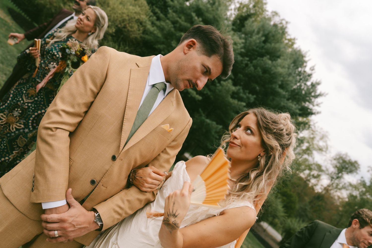 A romantic outdoor wedding moment captured in warm tones with a tan suit and white dress.