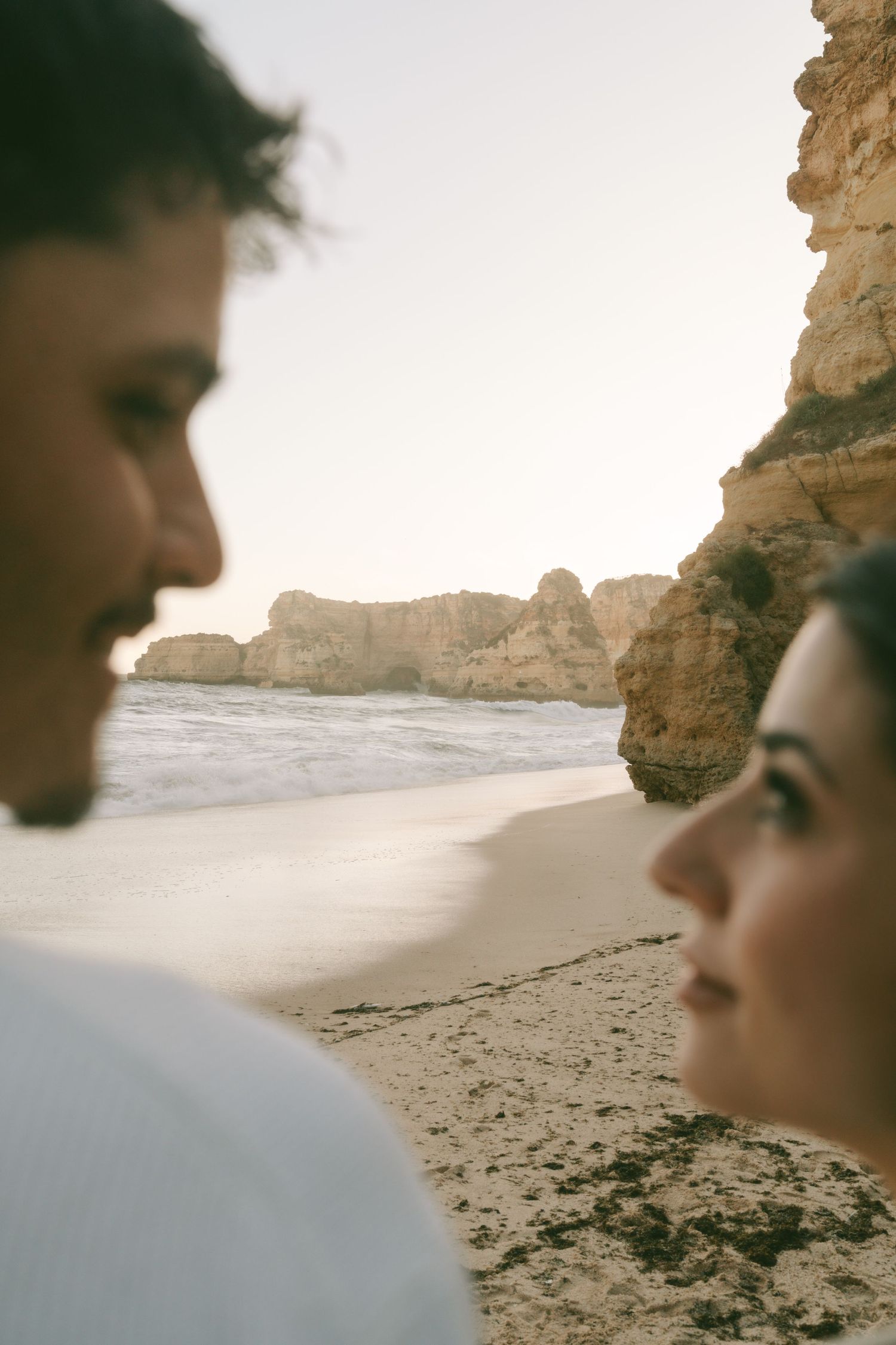 Close-up of a couple facing each other on an Algarve beach with golden rock formations and ocean in the background.