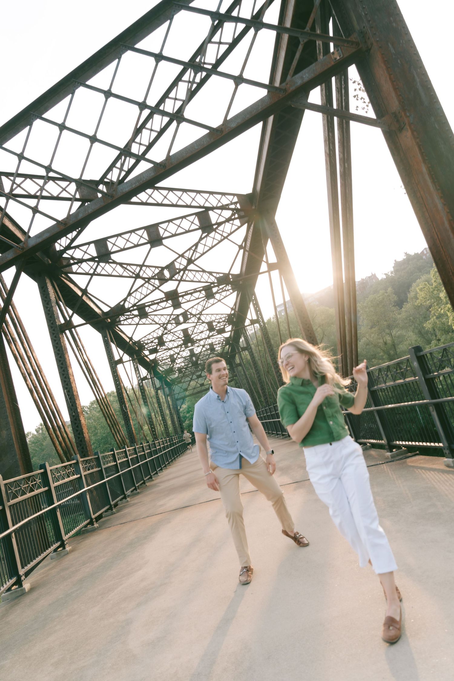 Two people dancing playfully on an old steel bridge during golden hour.