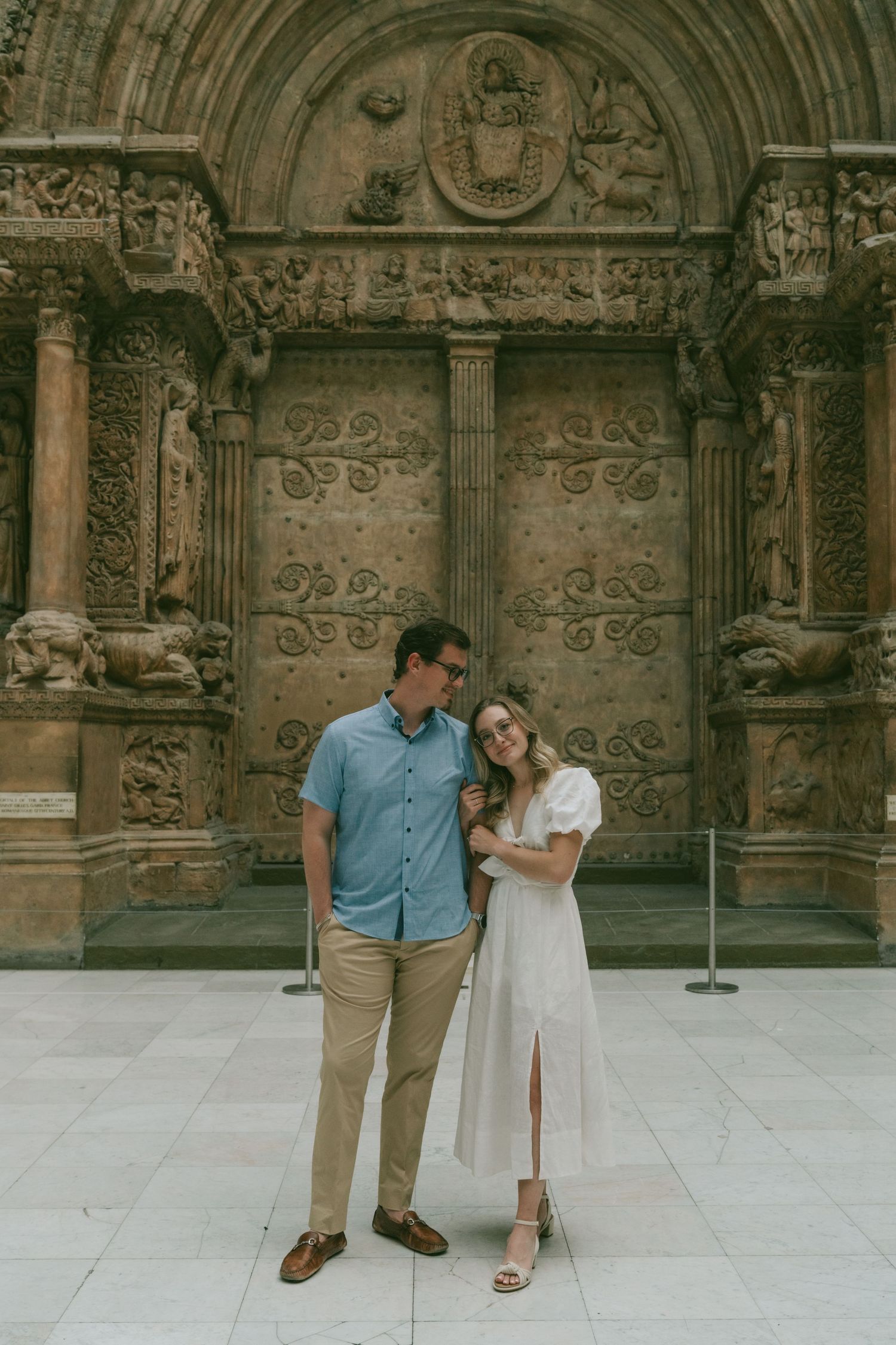 A couple explores the ornate stone architecture and carvings of a historic European building facade.