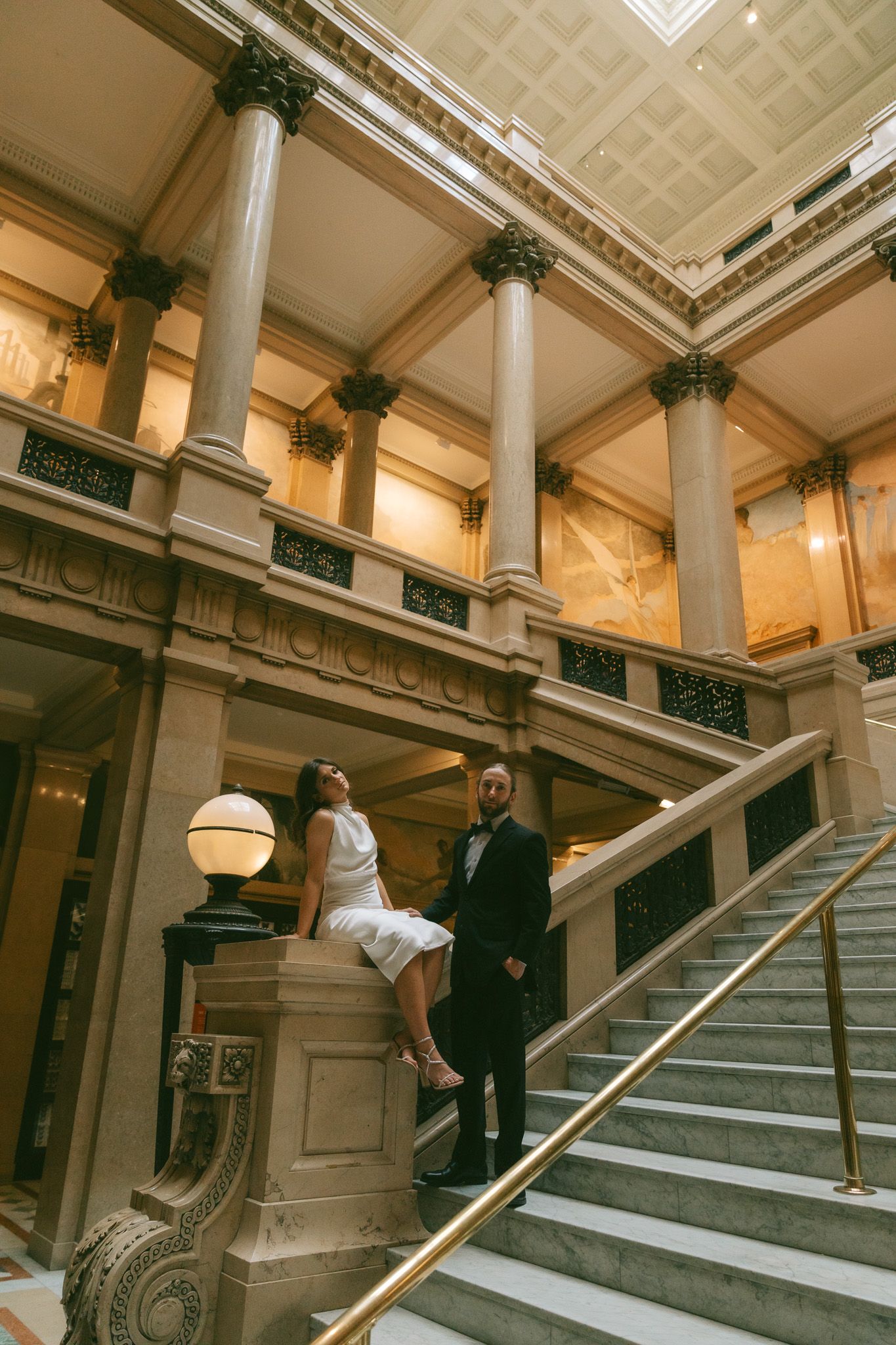 People pose dramatically on grand marble stairs in a historic building interior.