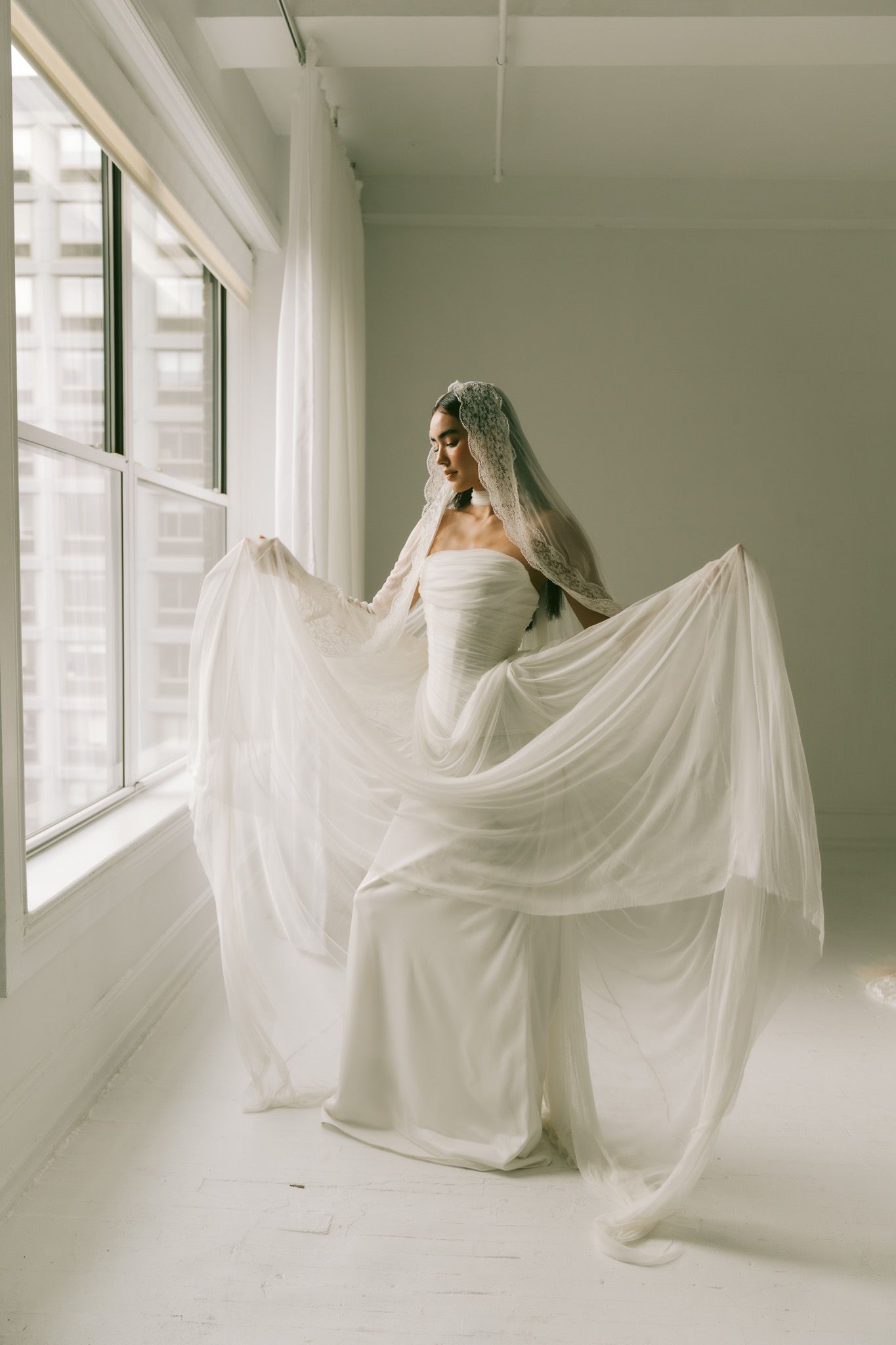 A figure draped in flowing white fabric dances gracefully through a bright minimalist studio space.