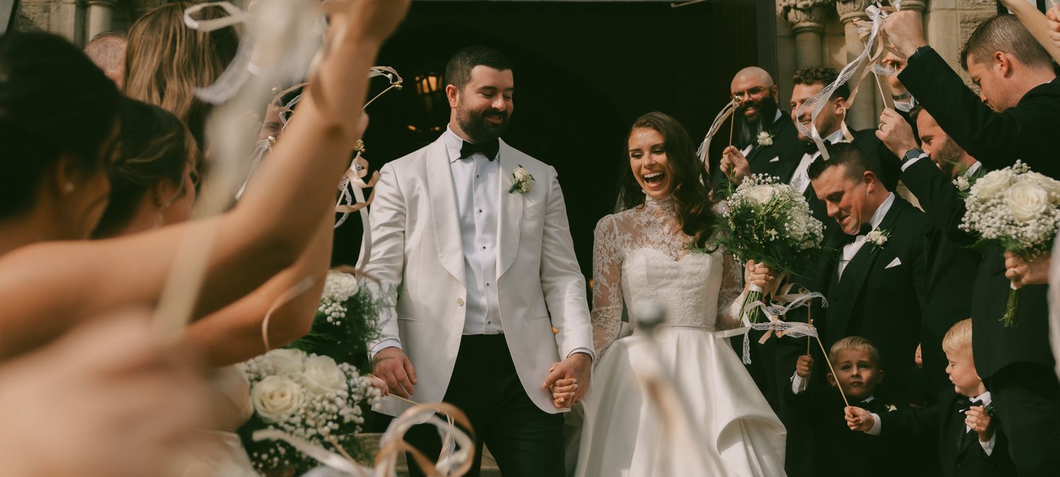Wedding party members in white and beige formal attire holding bouquets during celebration.