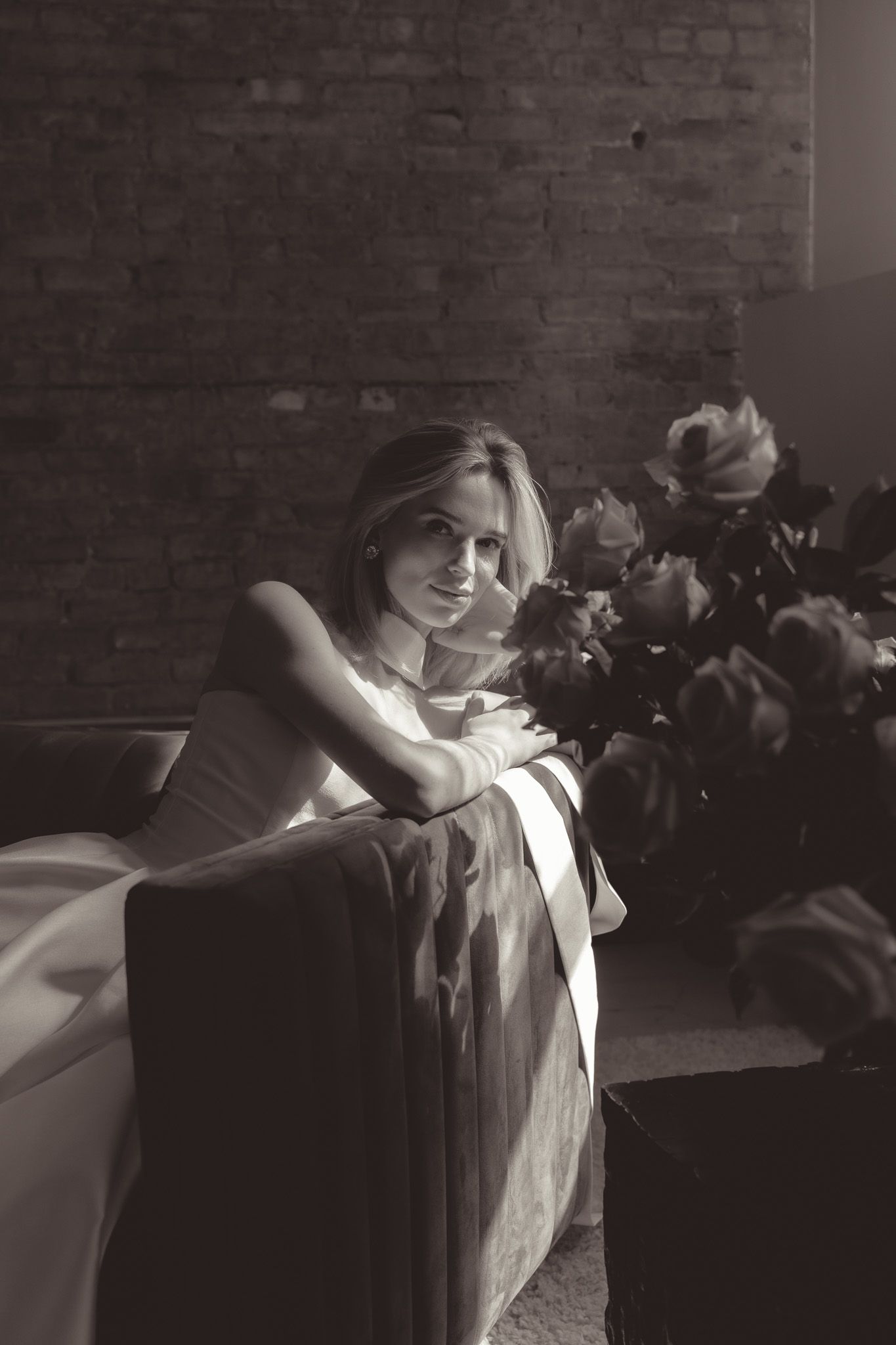 Black and white portrait with roses and exposed brick wall creating an elegant ambiance.