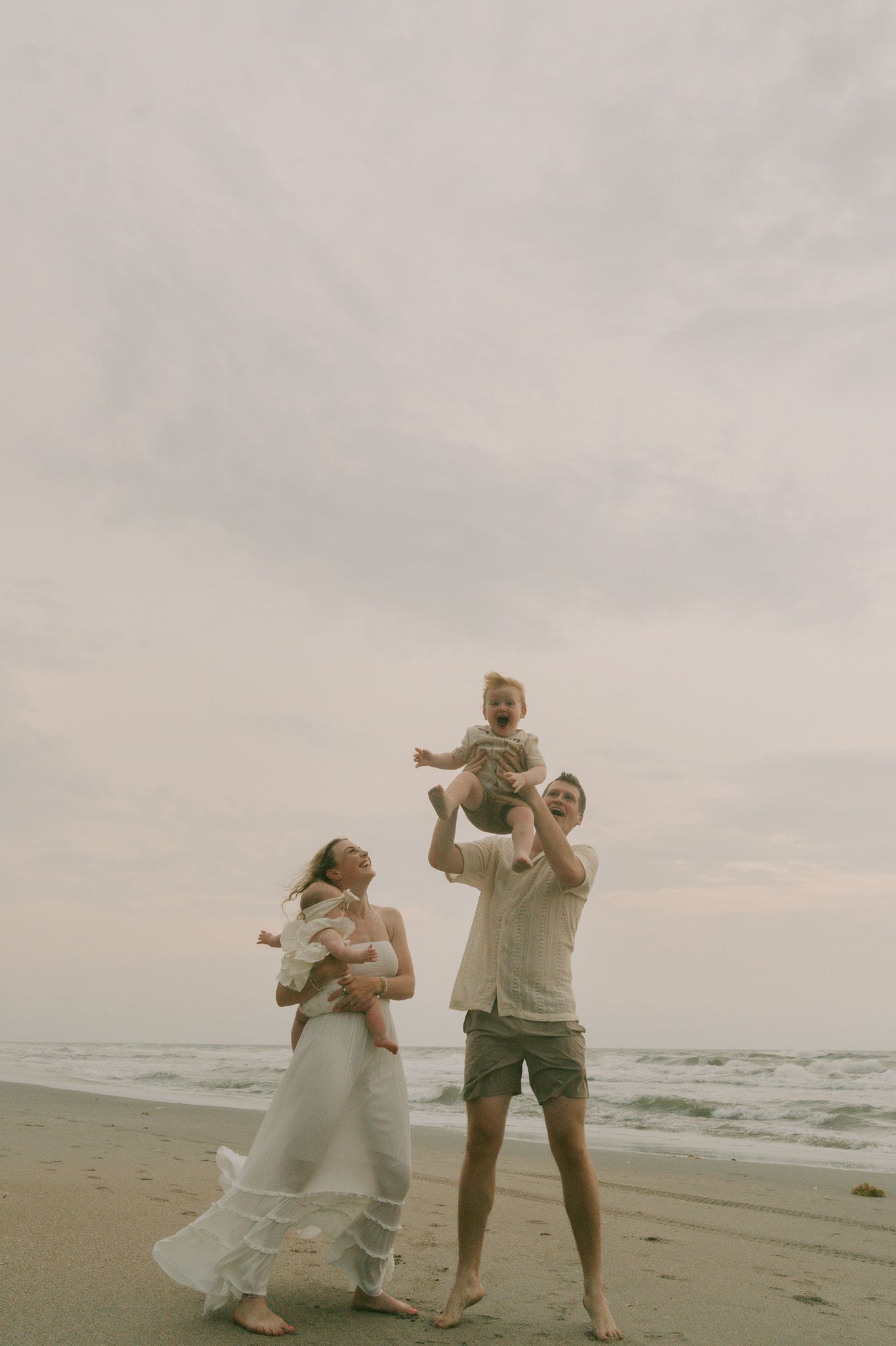Family playing together on beach at sunset with flowing white dress catching the breeze.