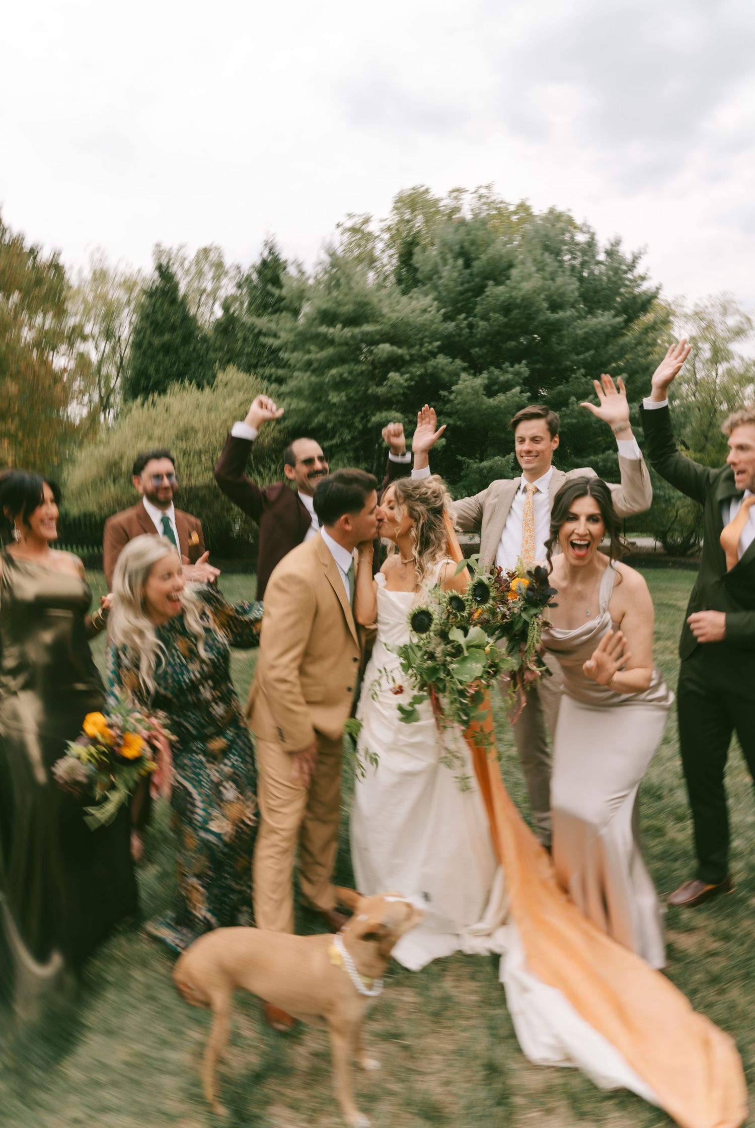 Wedding party members jump and celebrate together outdoors during a joyful photo session with autumn foliage.