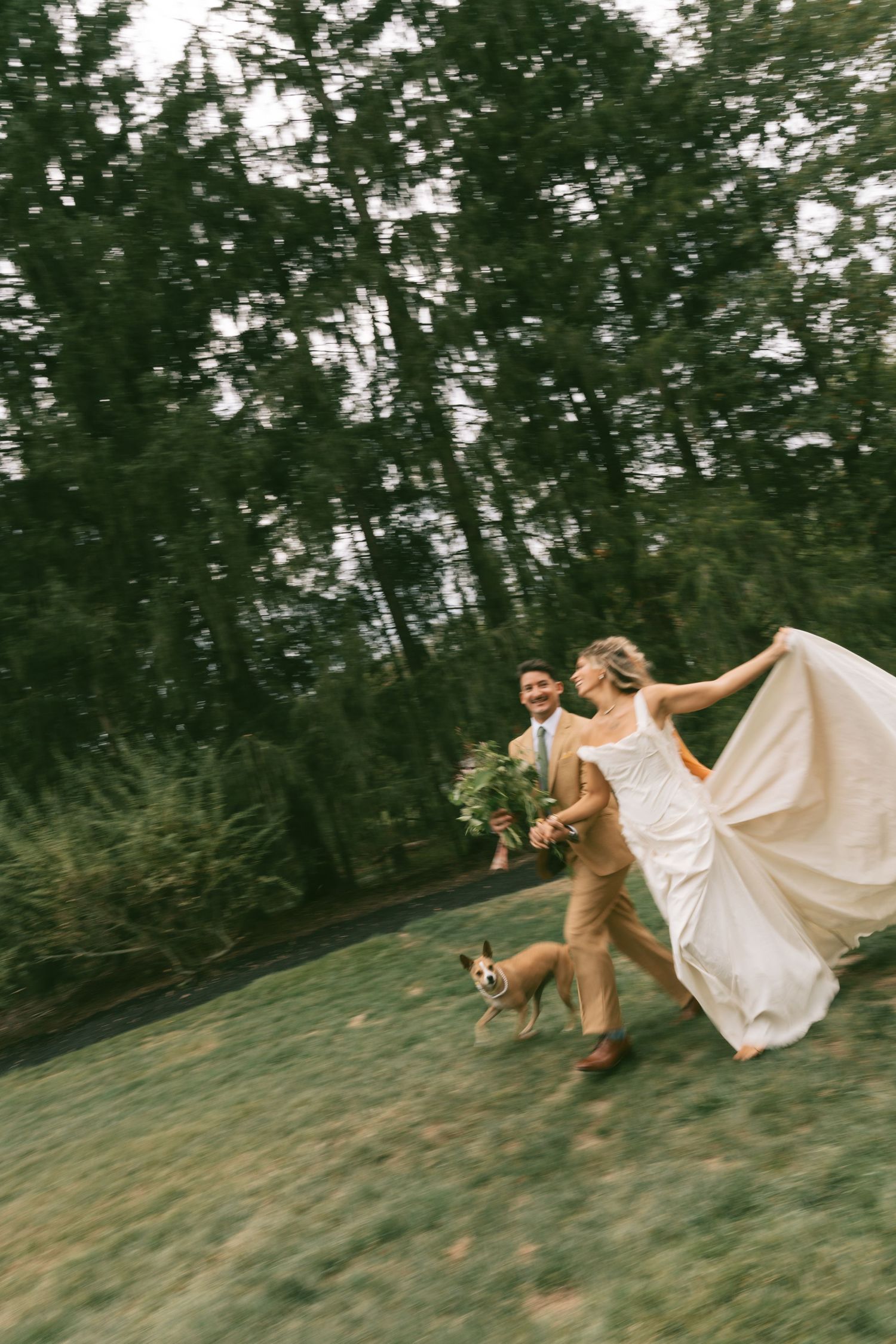 A playful scene of people running down a grassy hill in wedding attire.