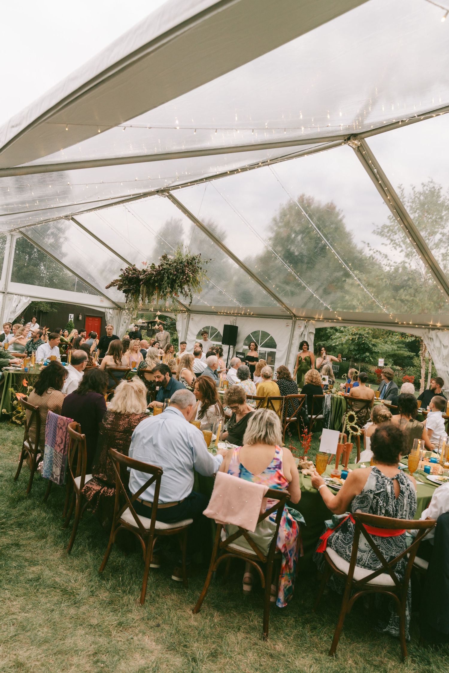 Wedding reception in a clear tent with guests seated at long tables for dinner.
