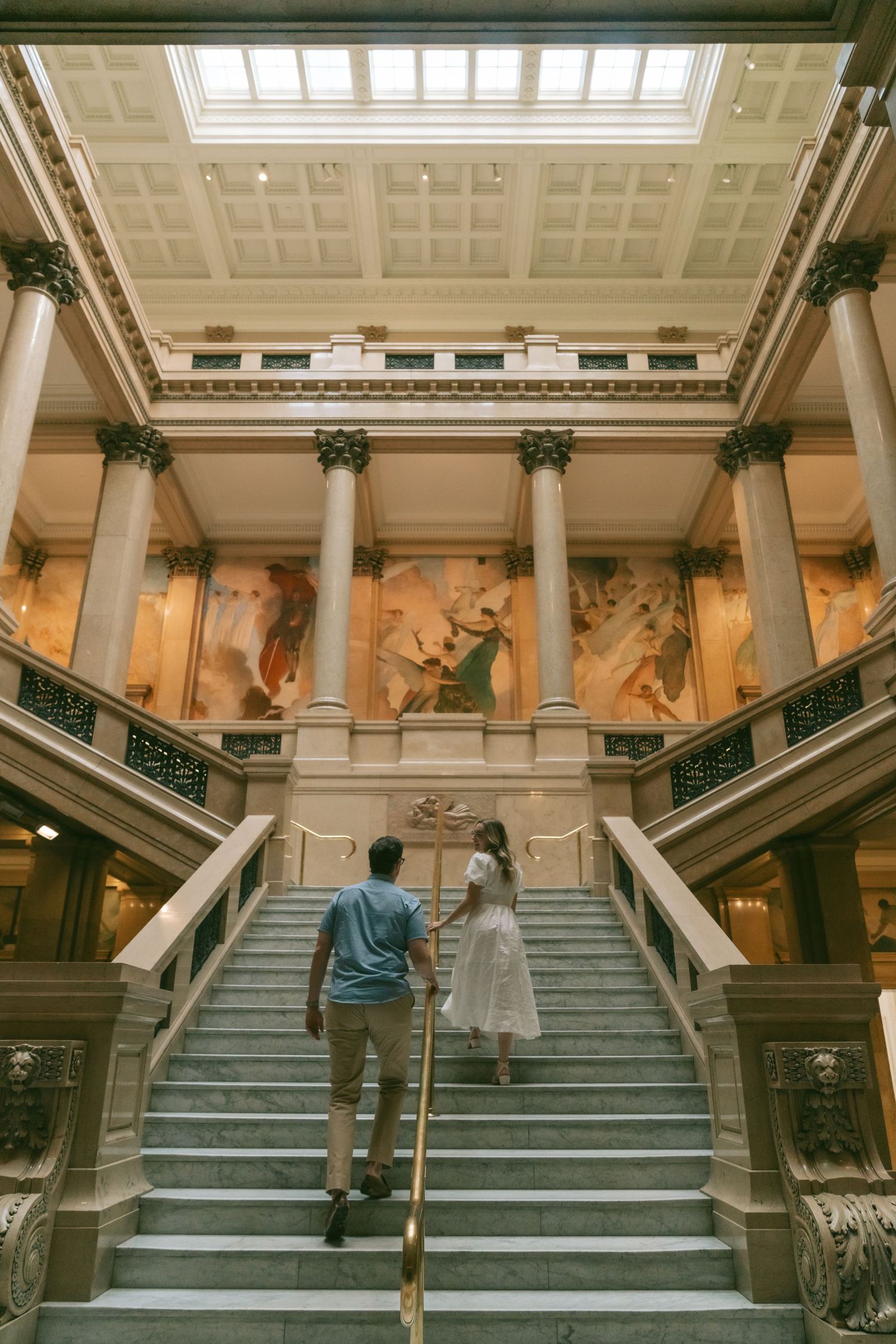 A grand interior staircase with classical columns and decorative murals in a historic museum or institution.