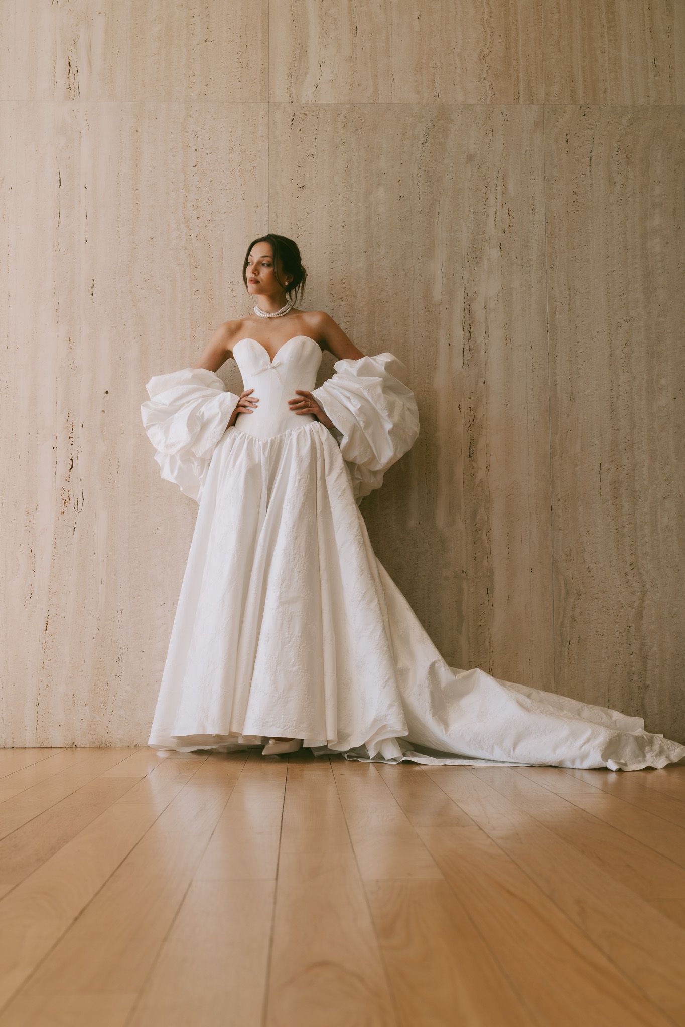 Dramatic white ball gown Eden Aharon wedding dress with statement puff sleeves and sweeping train against concrete backdrop in NYC.