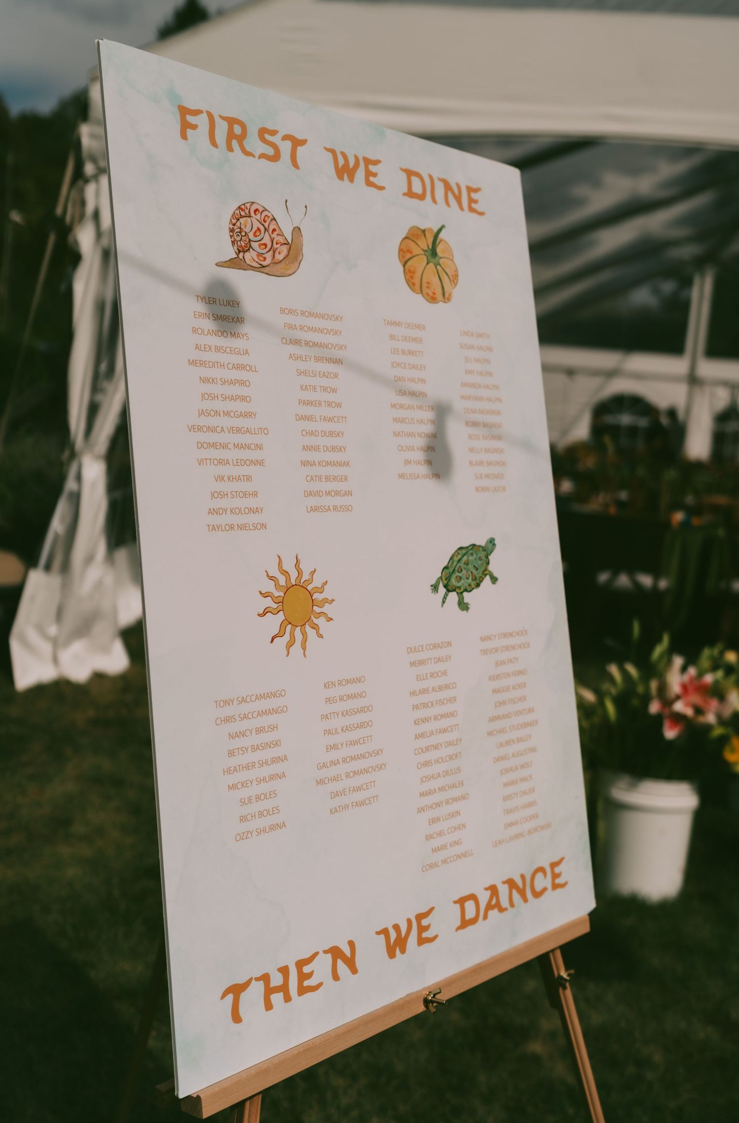 Wedding seating chart display with sun and turtle decorations showing table assignments for 'First We Dine Then We Dance'.
