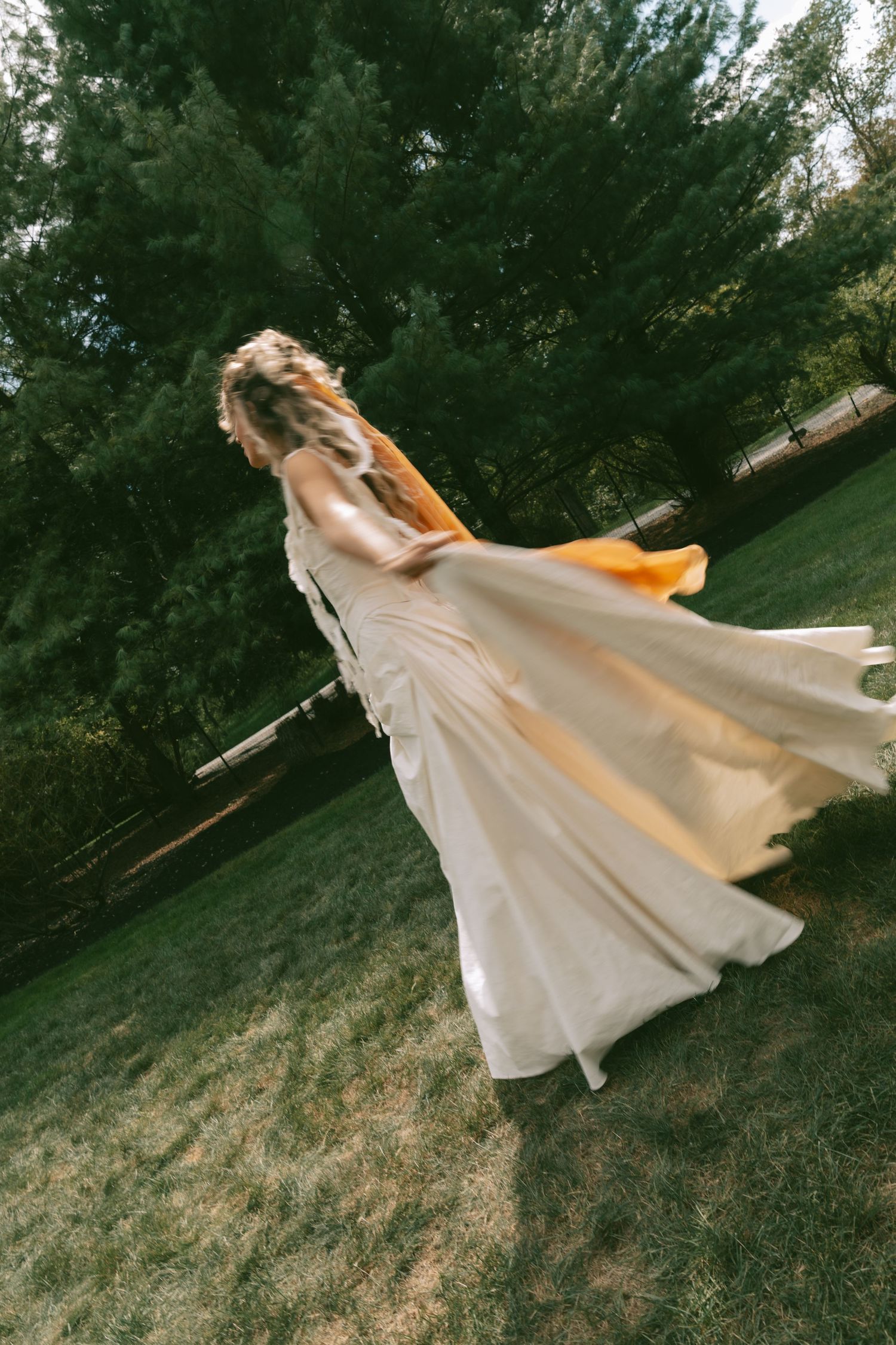 Person in flowing white dress twirls gracefully on grassy hillside at sunset.
