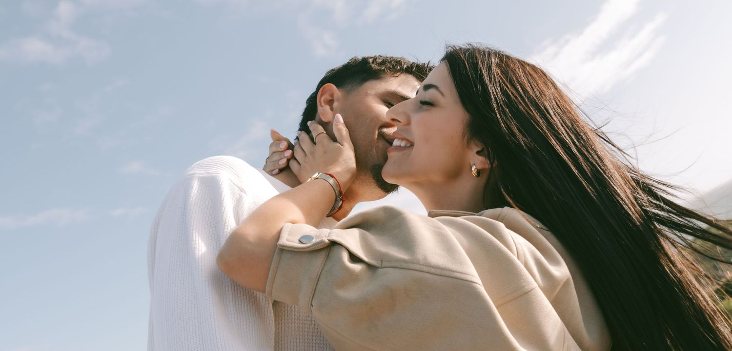 Romantic couple embracing and sharing a tender moment under a bright blue sky outdoors.