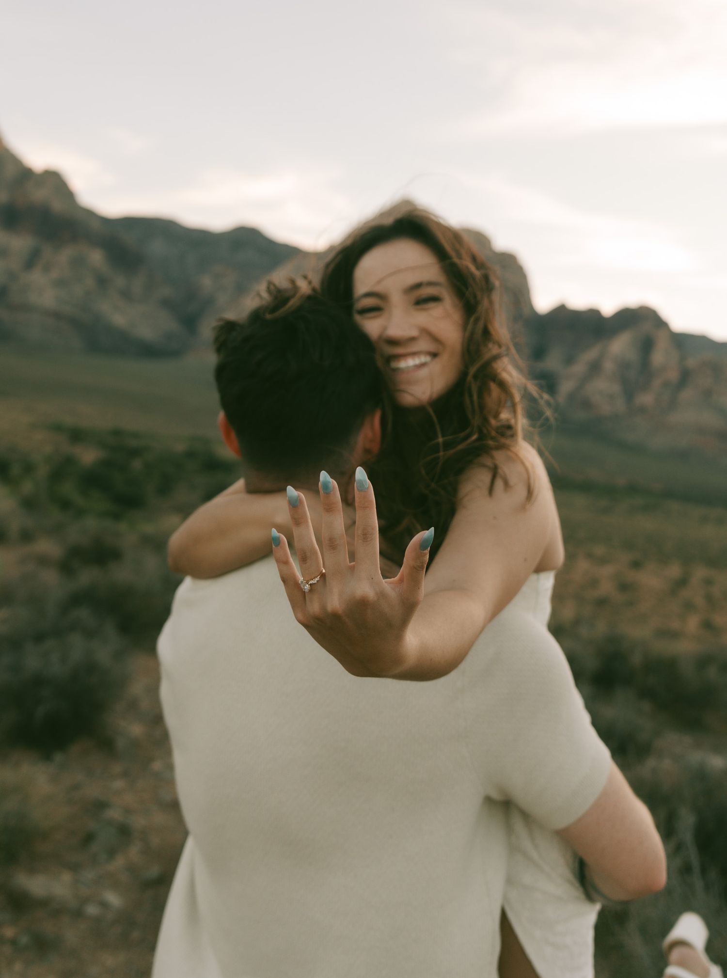 A couple embraces outdoors with mountains in the background during a joyful moment at sunset in red rock canyon, las vegas.