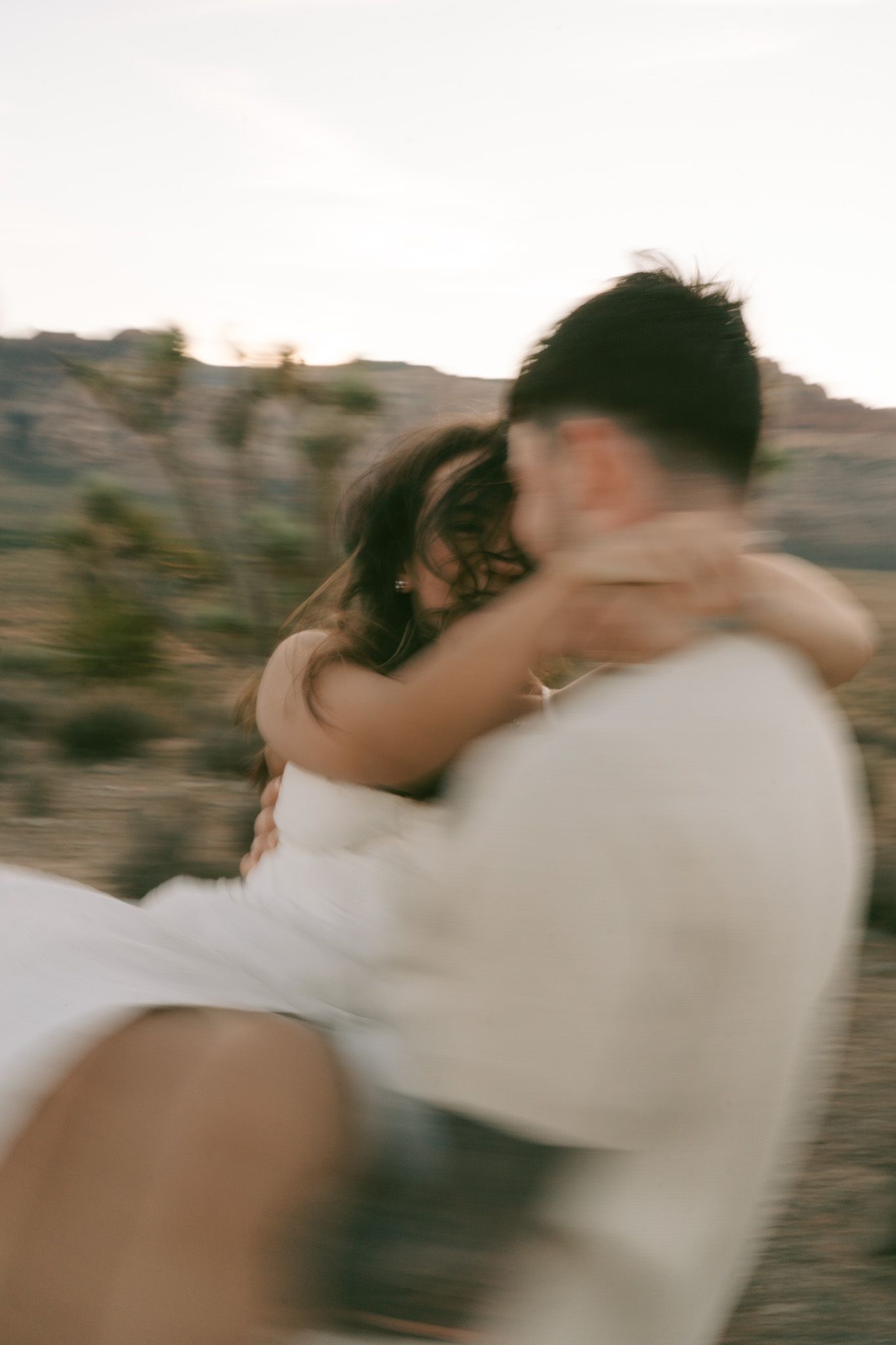 A couple in casual clothing share an intimate moment in front of a desert landscape at sunset in red rock canyon, las vegas.