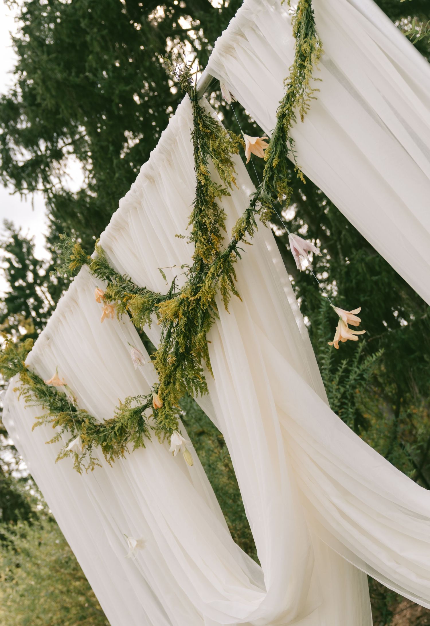 White fabric draping decorated with greenery garlands creates an elegant outdoor wedding backdrop.