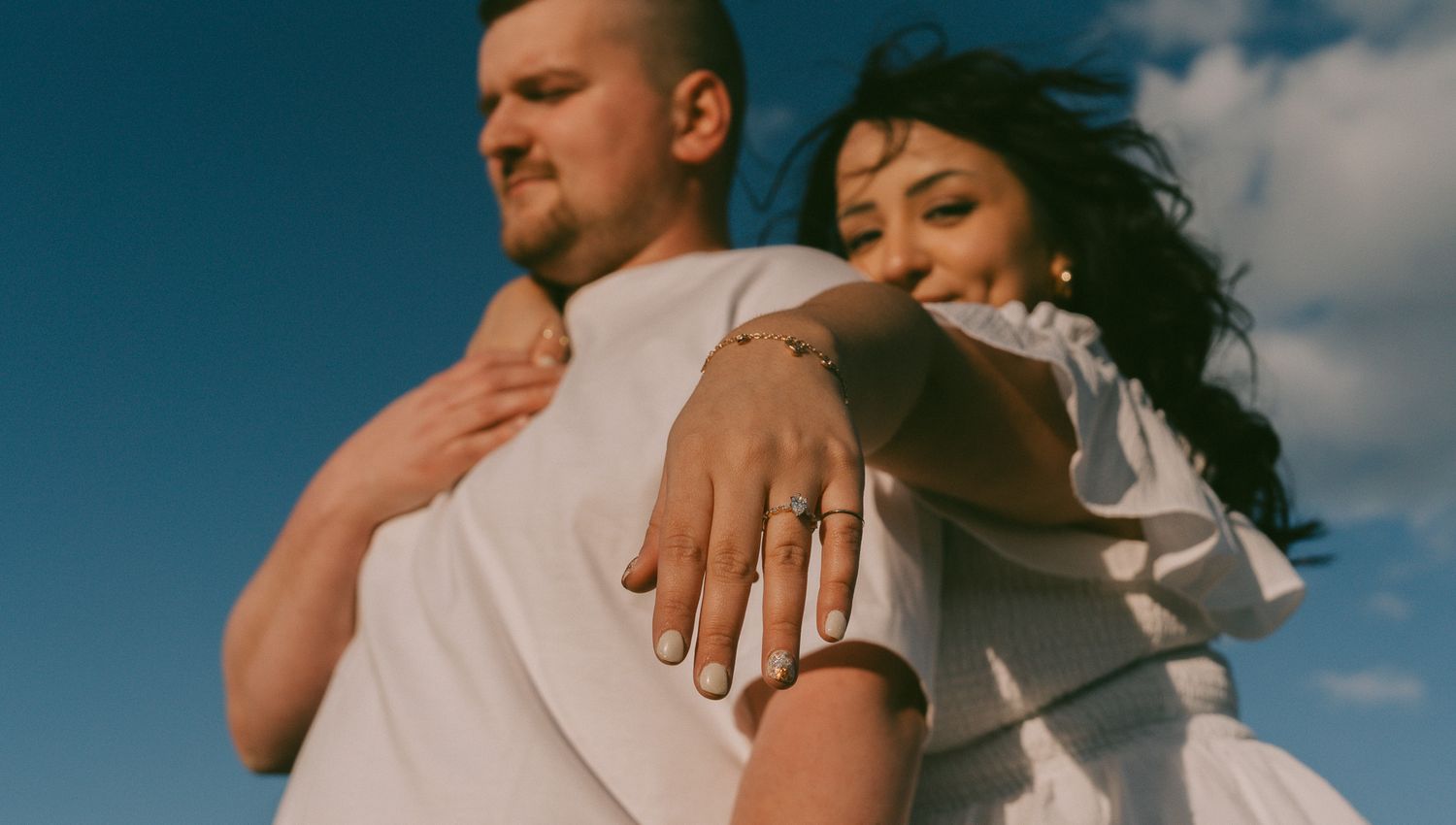 Close-up shot of an embrace showing a wedding ring against a blue sky.
