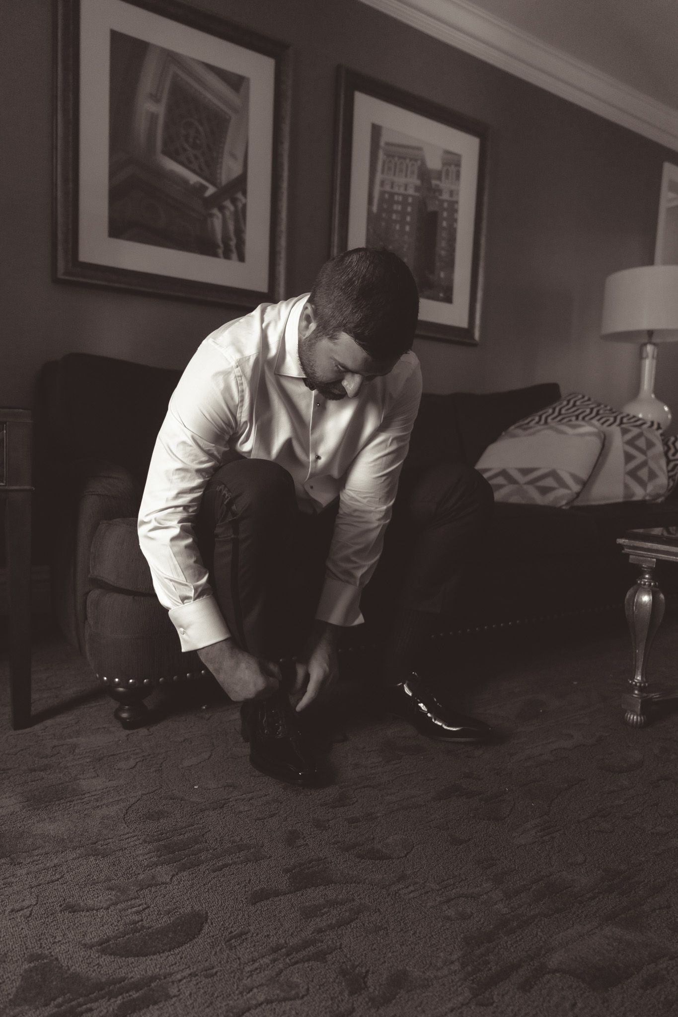 Man in white dress shirt crouches low to examine something on patterned carpet in dimly lit room in downtown pittsburgh, pa.