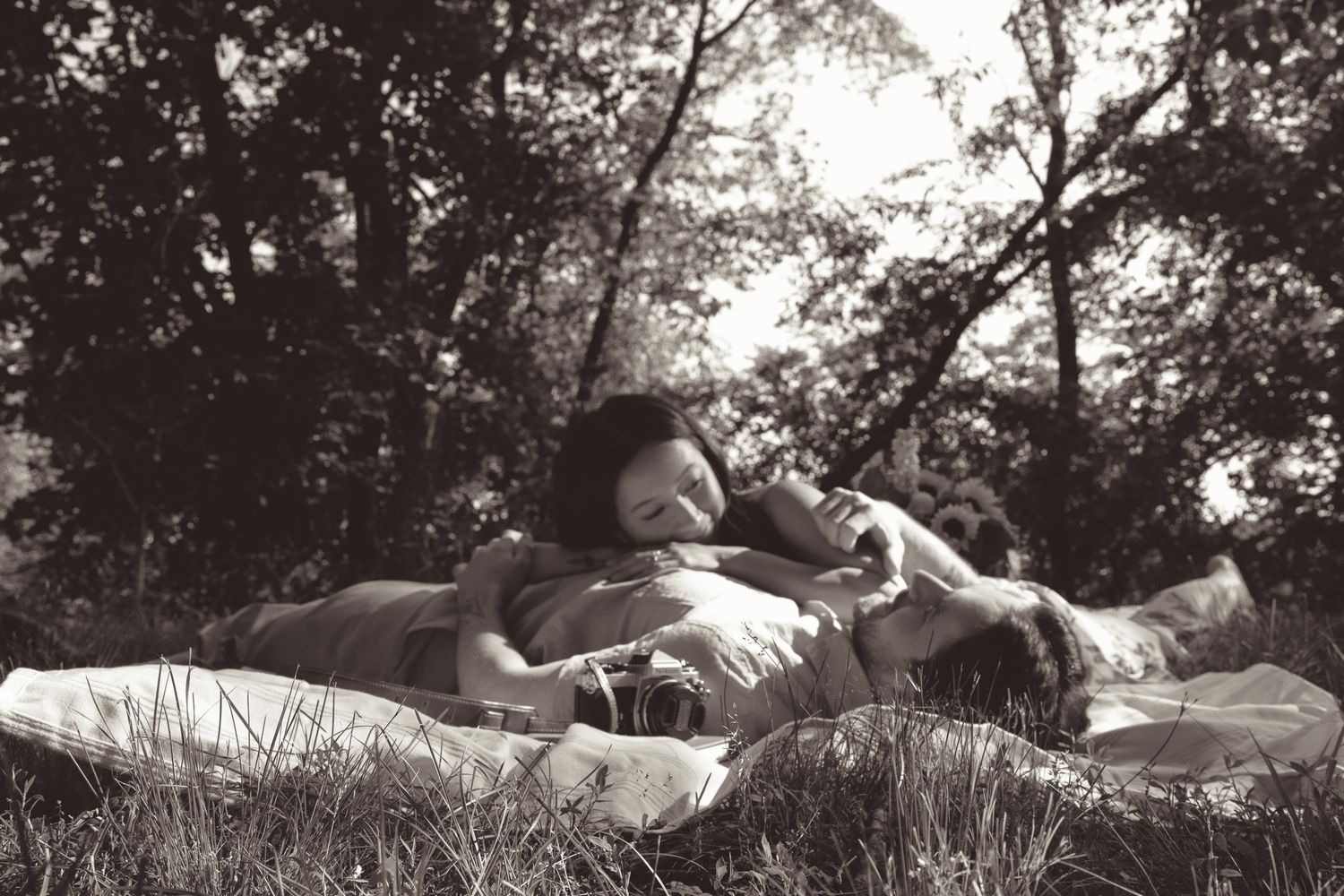 A couple rests together on blankets in a peaceful woodland setting, captured in black and white photography in pittsburgh