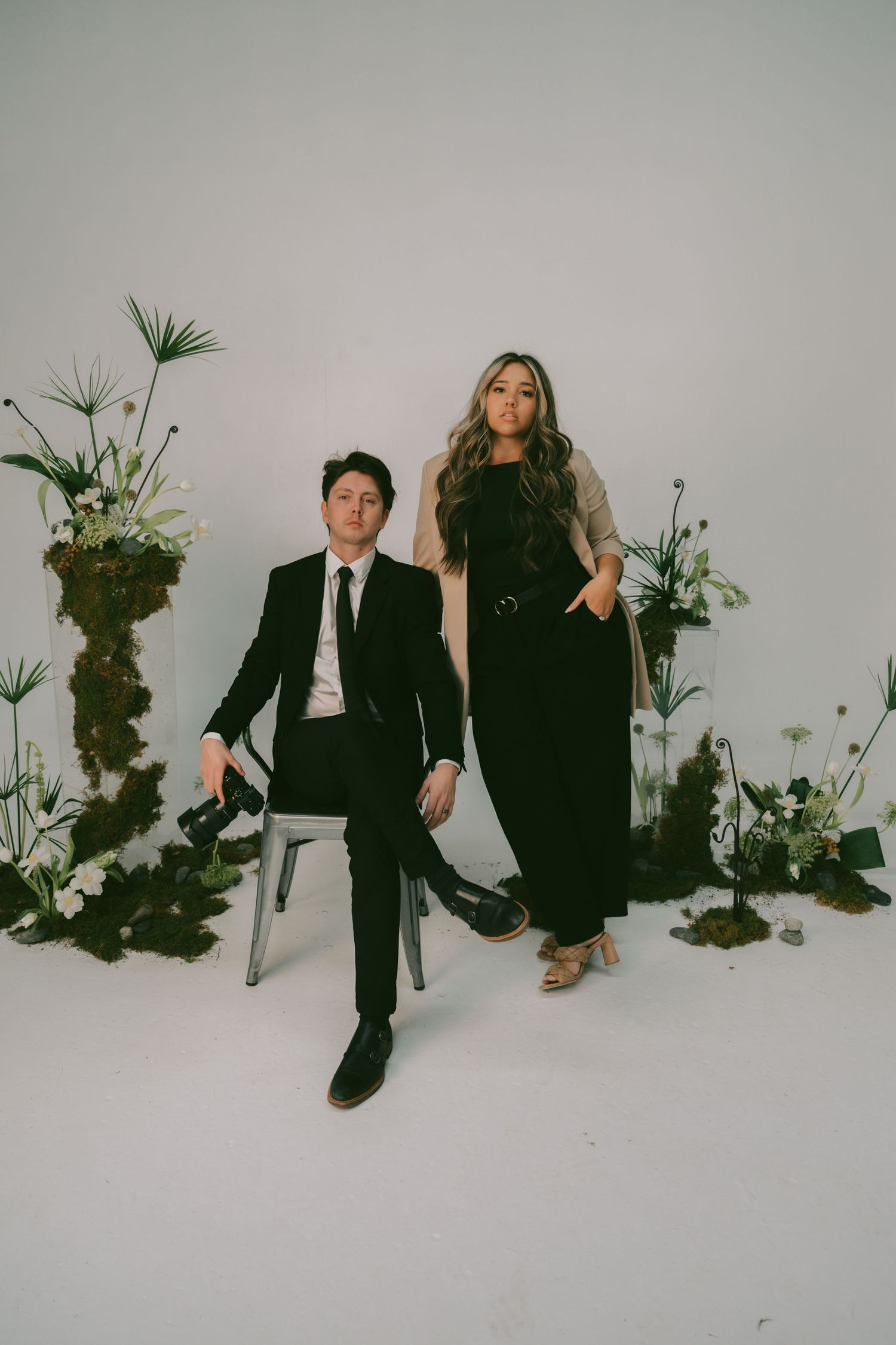 A stylish studio portrait with floral arrangements against a light gray backdrop.