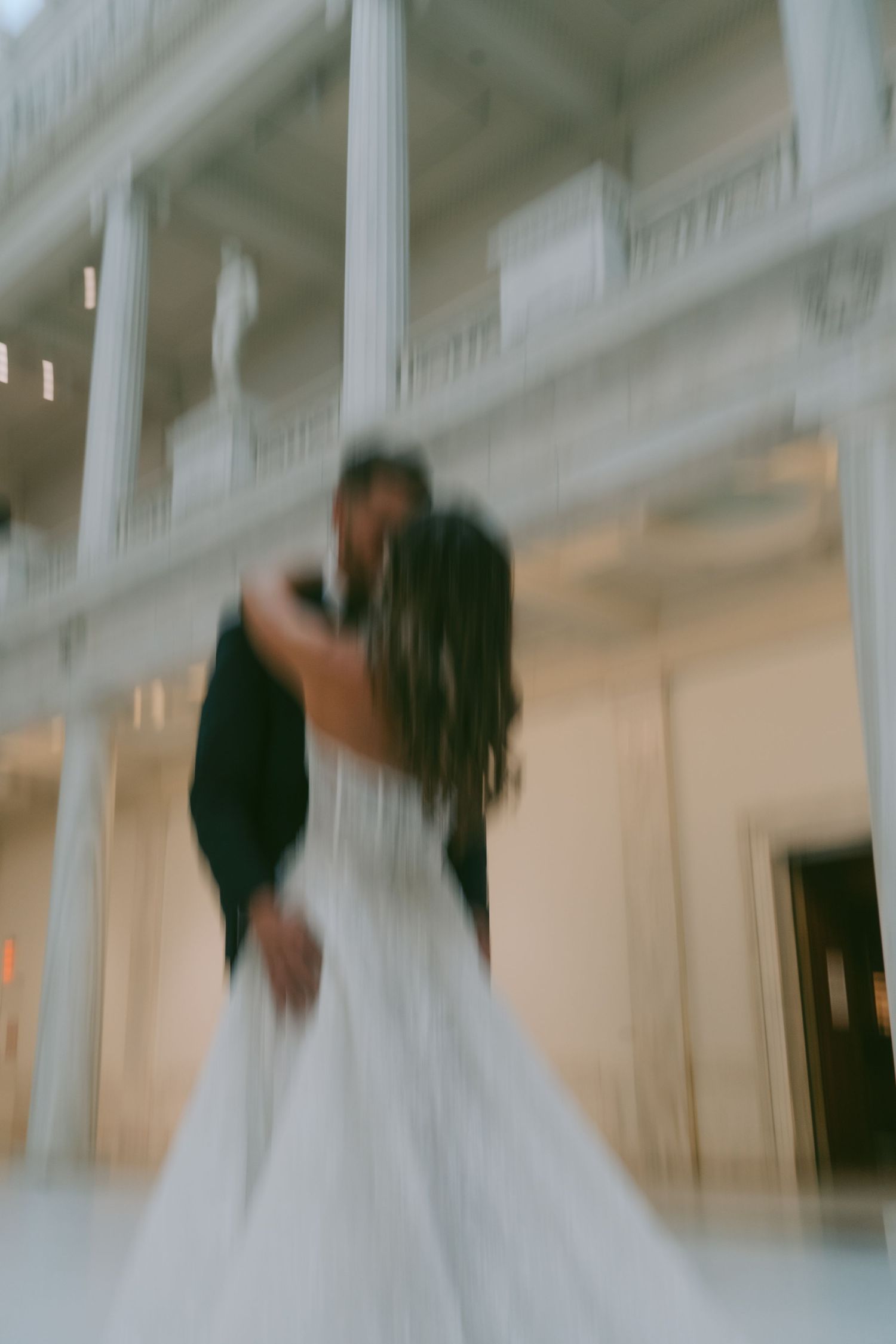 A blurred motion sequence of a couple in wedding attire dancing in an elegant white ballroom.