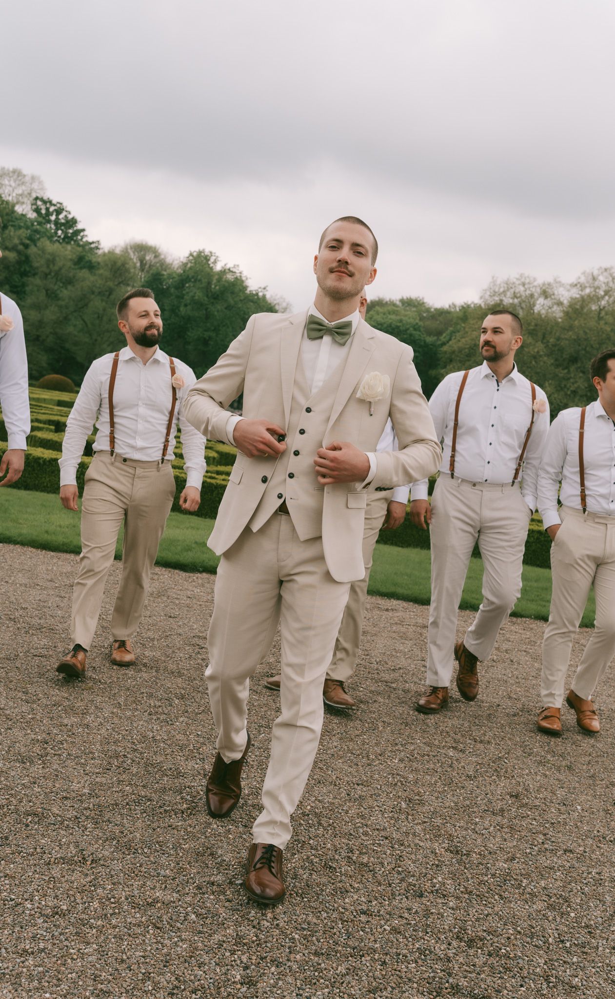Group of groomsmen in light suits and suspenders walking outdoors in Germany.